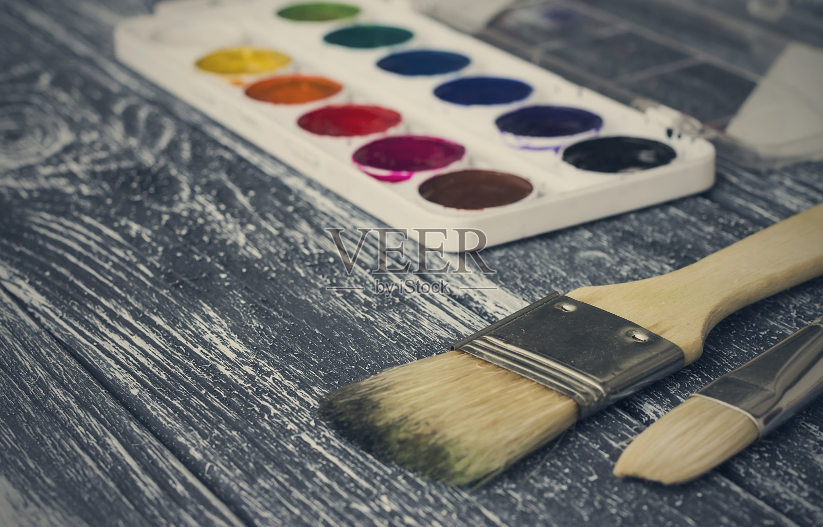 旧桌子上放着调色板，上面有水彩颜料和画笔。照片摄影图片