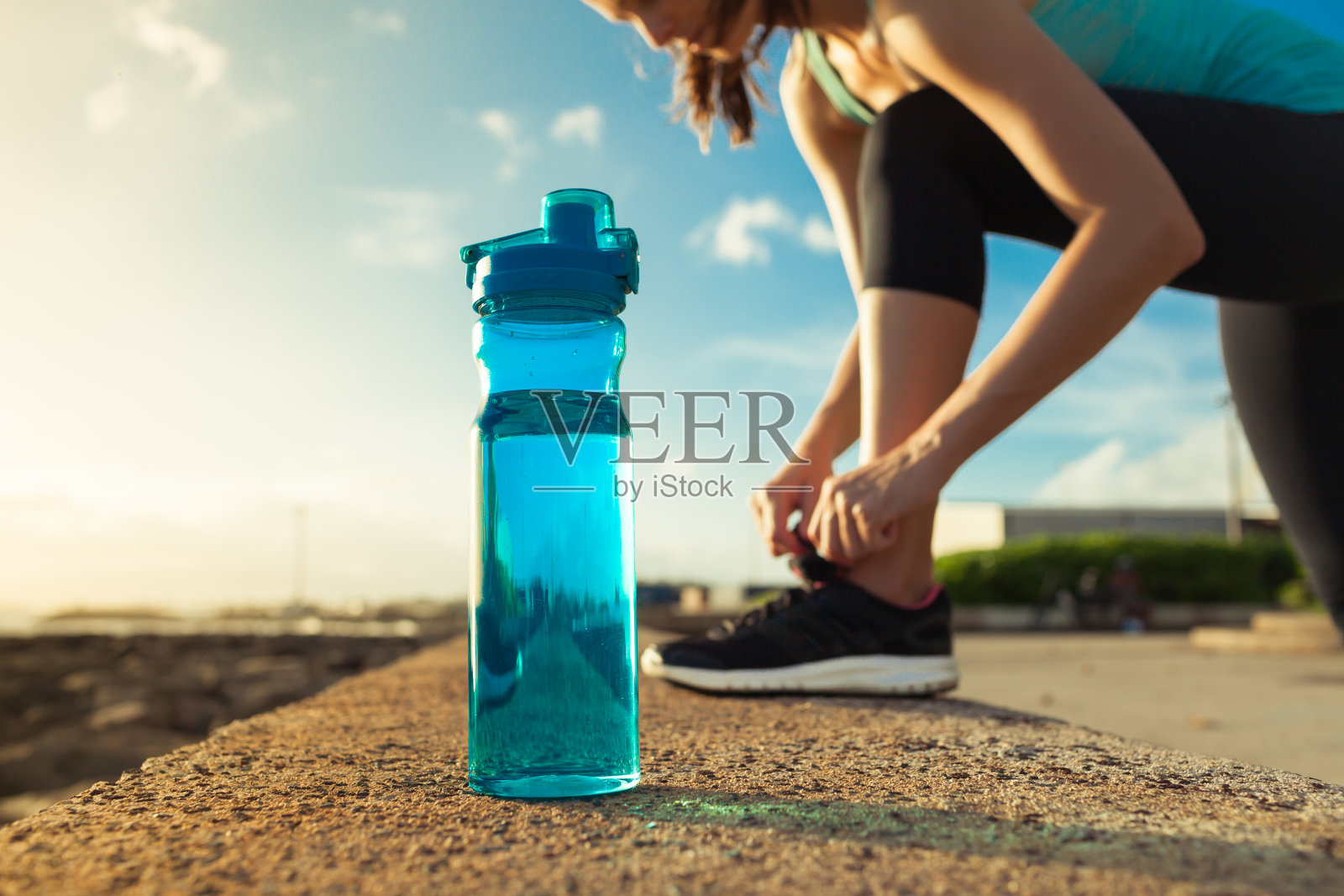 女跑步者系着她的鞋子旁边的一瓶水照片摄影图片