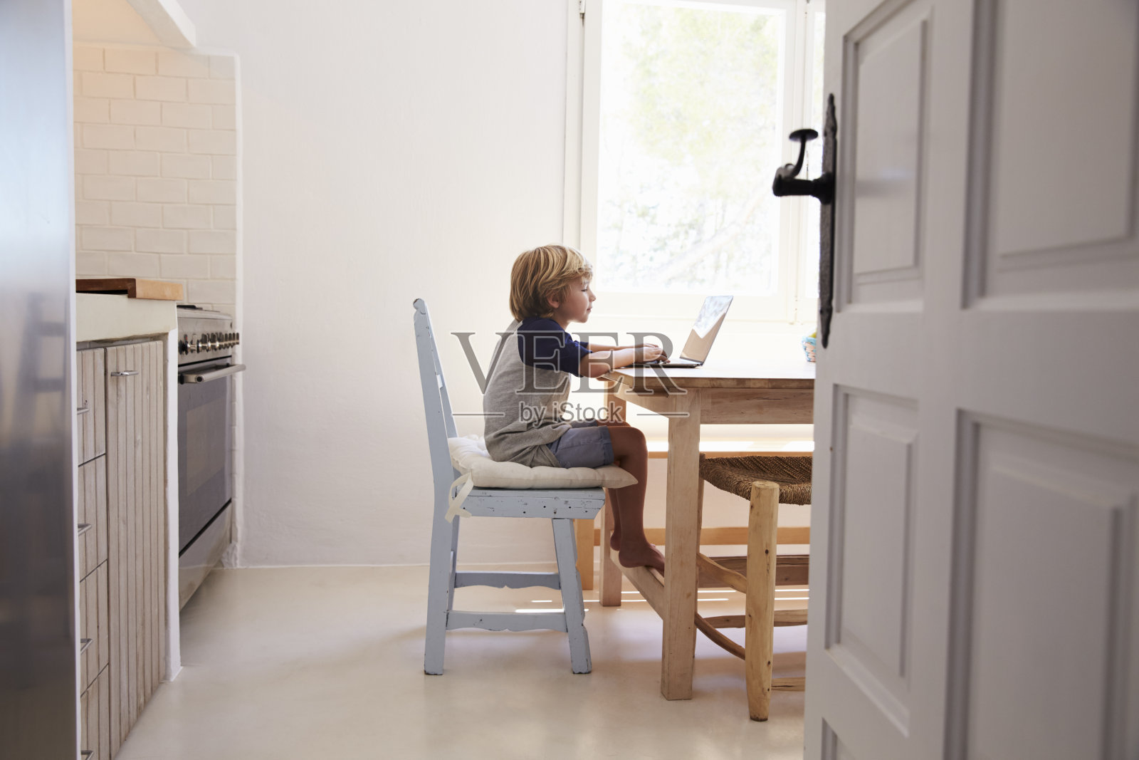 小男孩在厨房用笔记本电脑，从门口的侧视图照片摄影图片