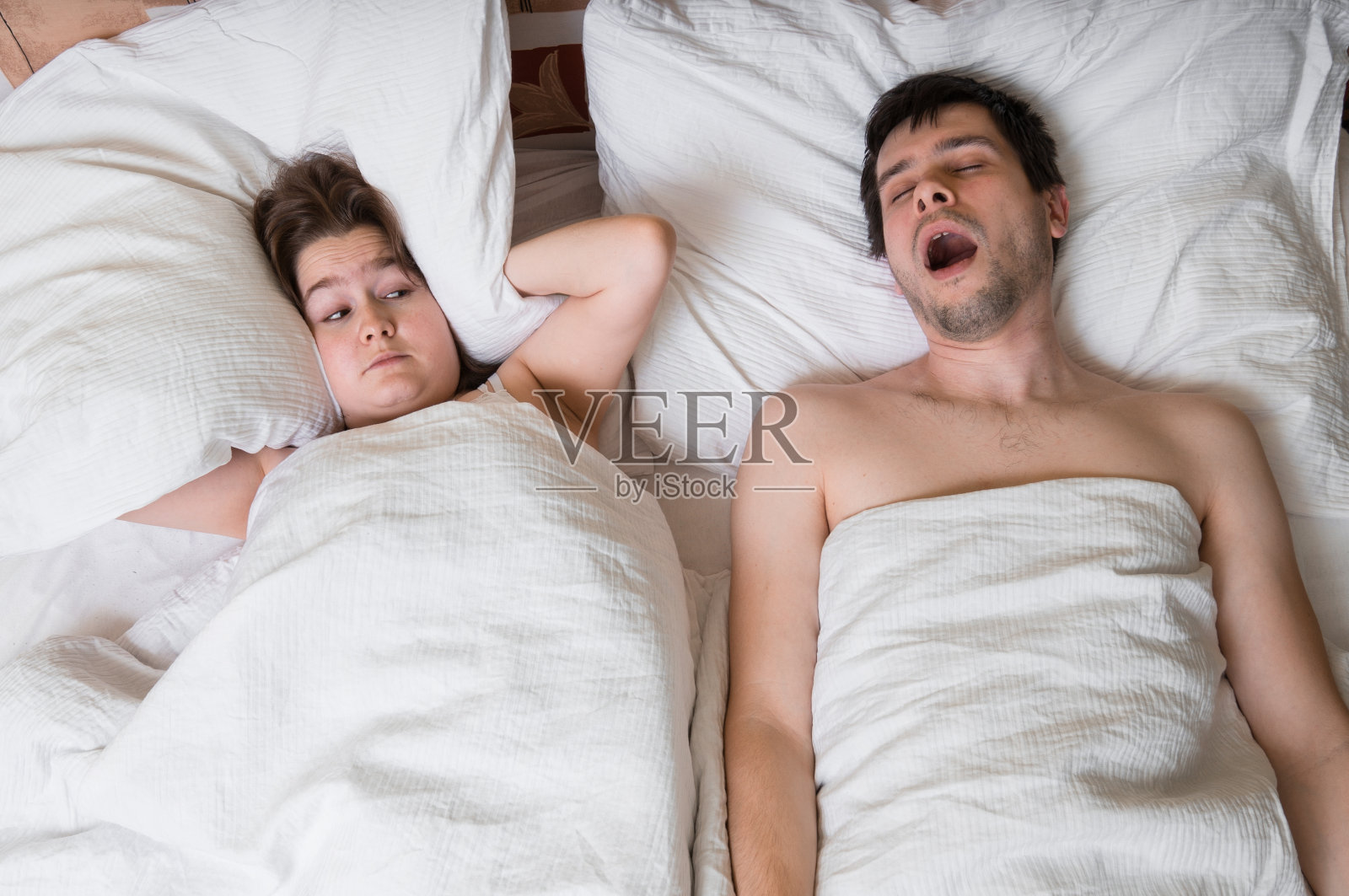 一对夫妇躺在床上。打鼾的男人和捂耳朵的女人。照片摄影图片