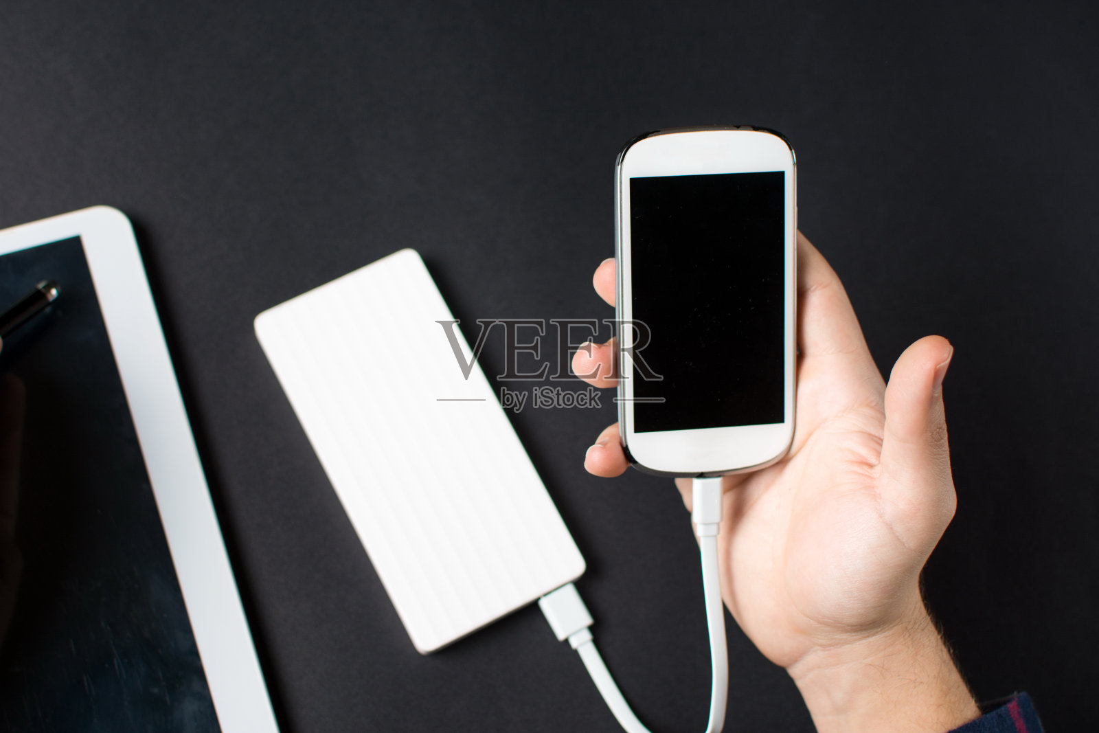 男性的手拿着一个连接电源的白色手机照片摄影图片