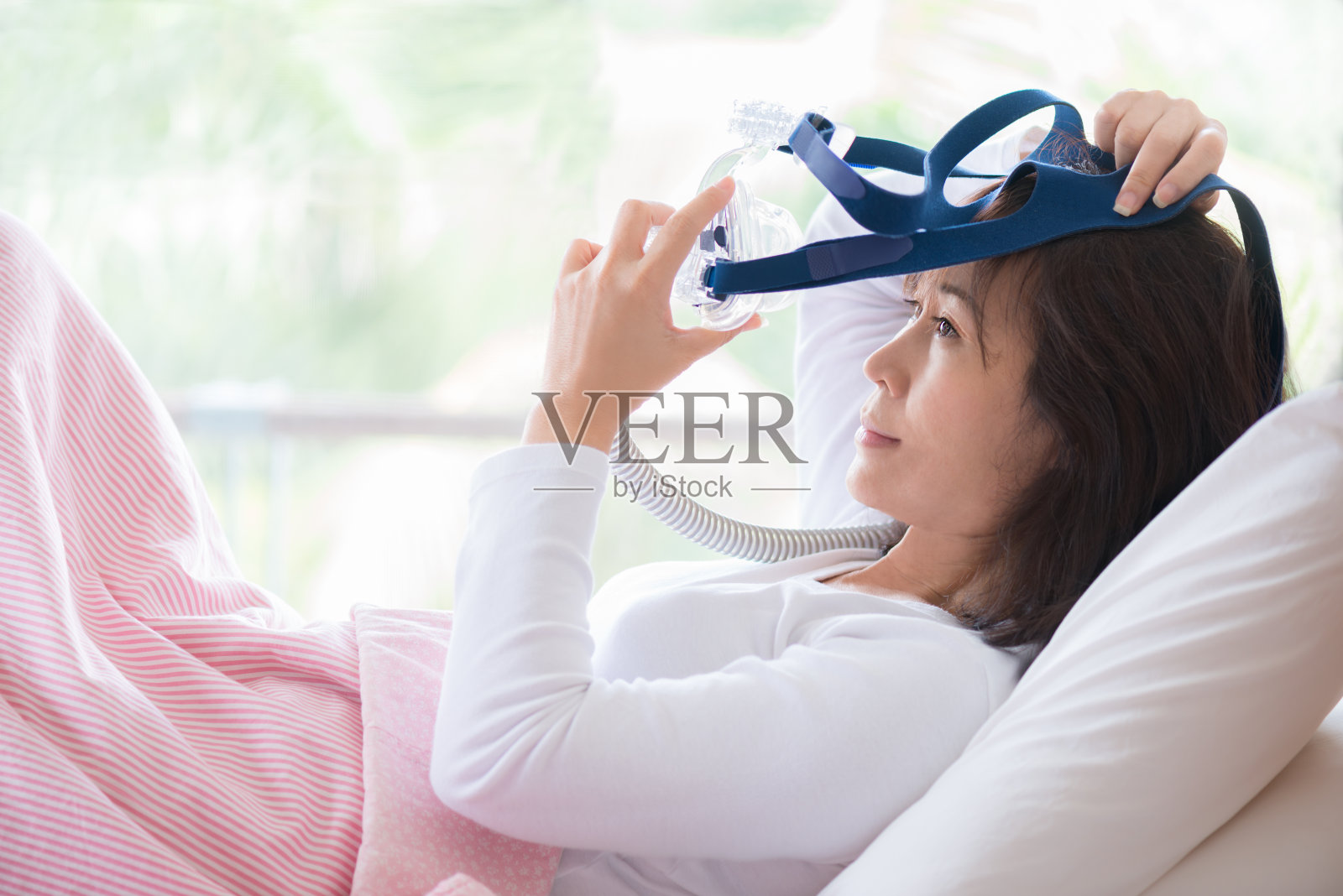 一个女人躺在床上戴着呼吸面罩，接受睡眠呼吸暂停治疗照片摄影图片
