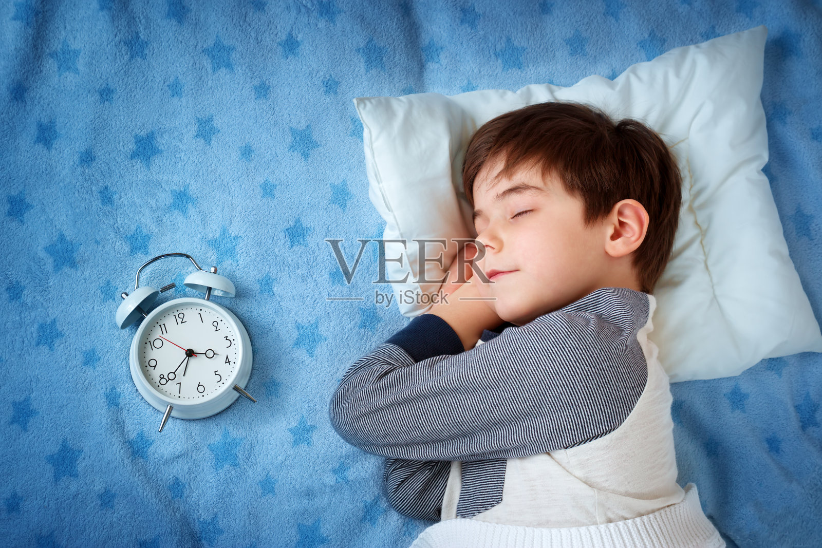 6岁的孩子睡在有闹钟的床上照片摄影图片