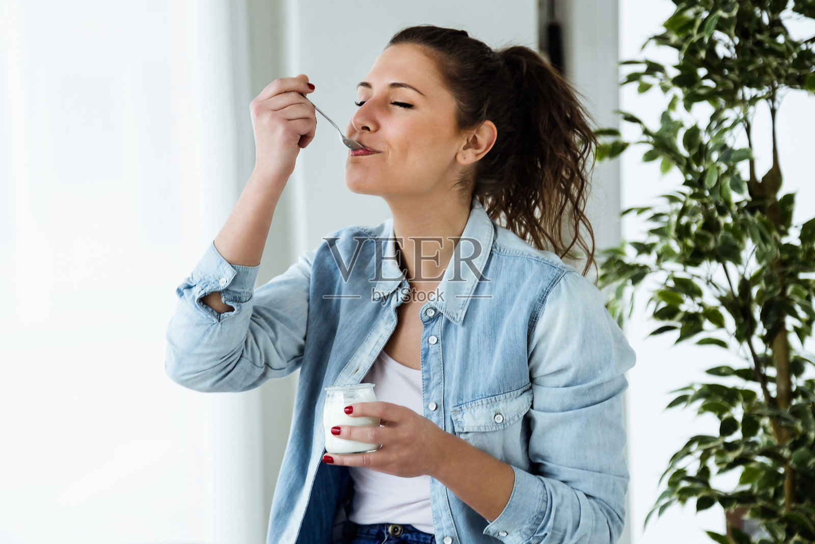 年轻漂亮的女人在家里吃酸奶。照片摄影图片