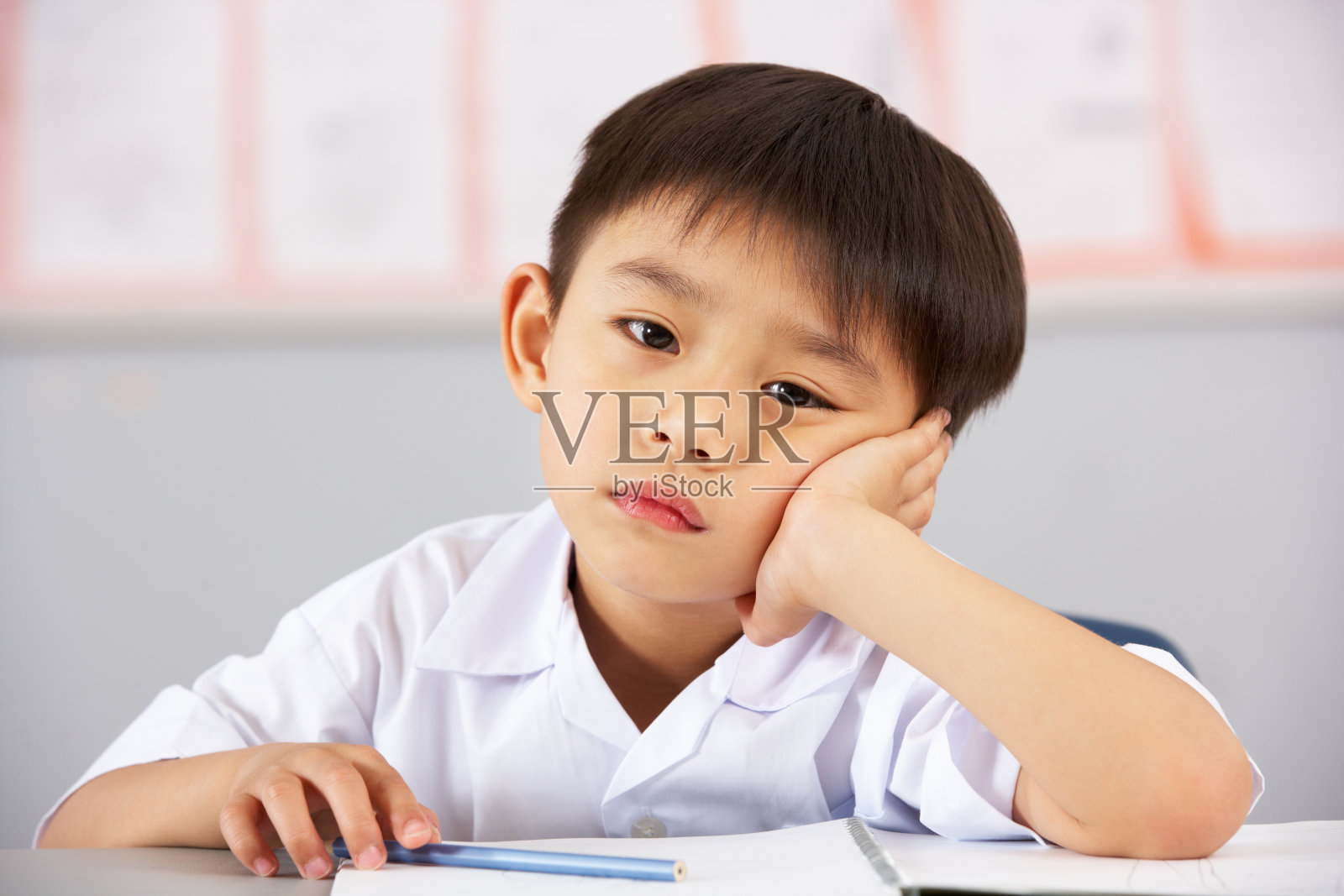 在中国学校的课桌上工作的不快乐的男学生照片摄影图片