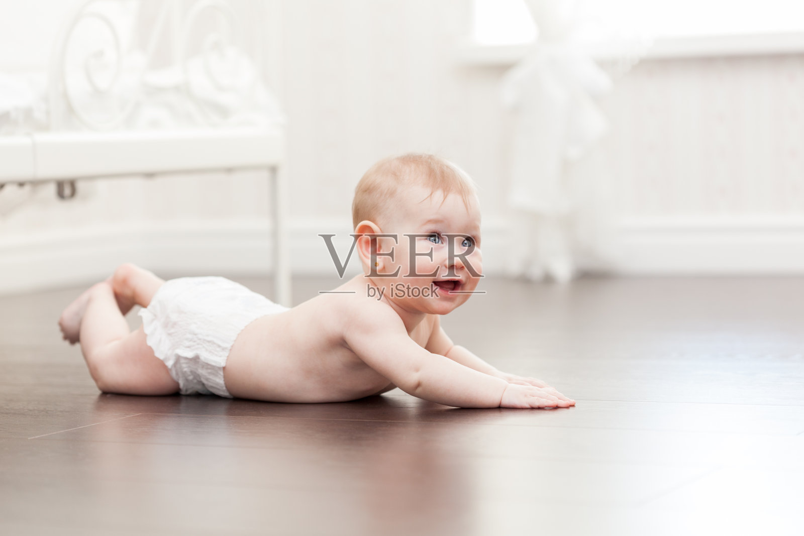 快乐的7个月大的小女婴在硬木地板上爬照片摄影图片