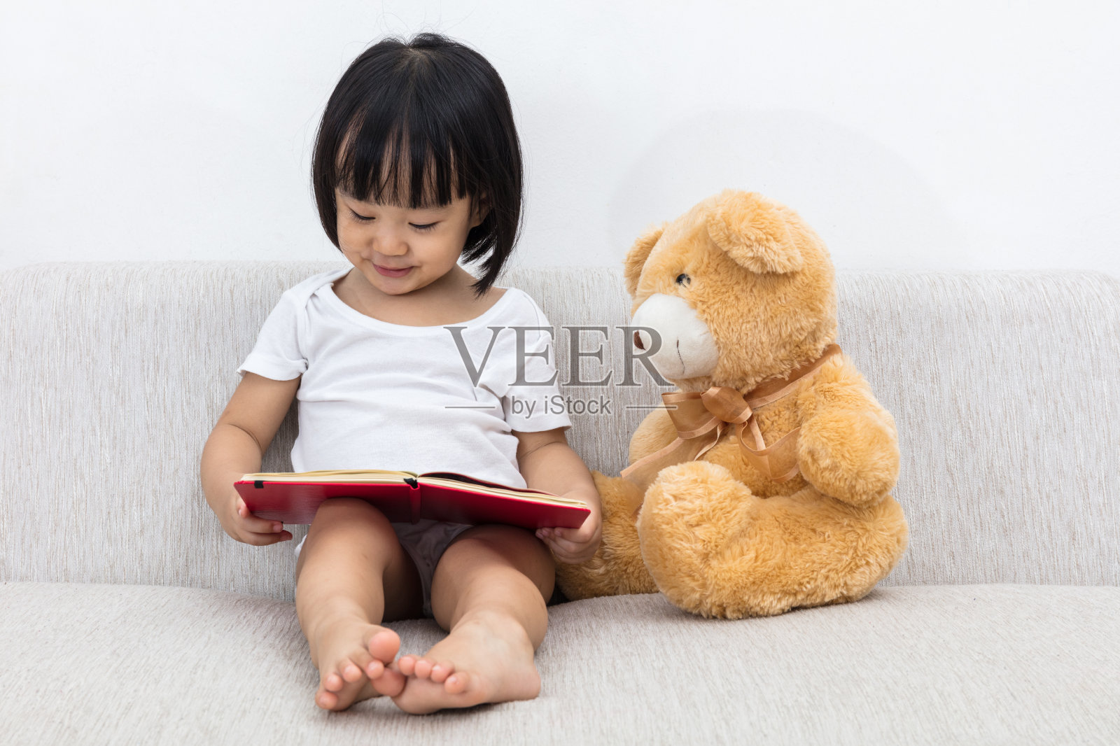 亚洲华人小女孩和泰迪熊一起看书照片摄影图片
