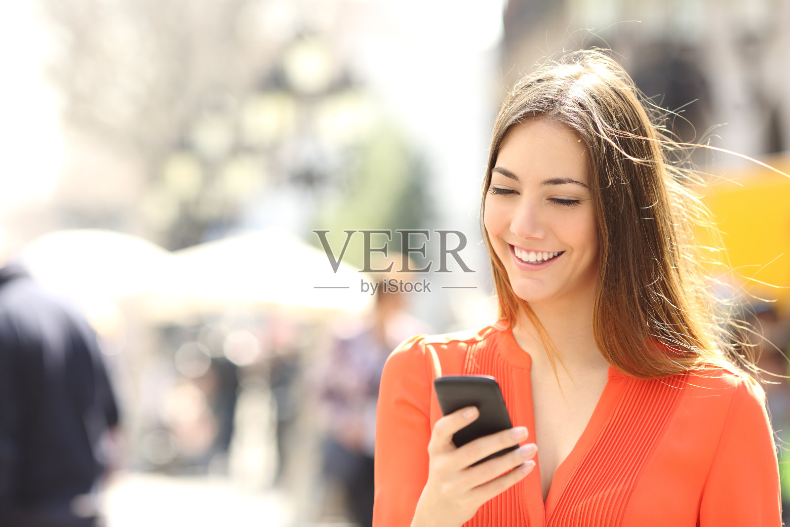 穿橘色衬衫的女人在用智能手机发短信照片摄影图片