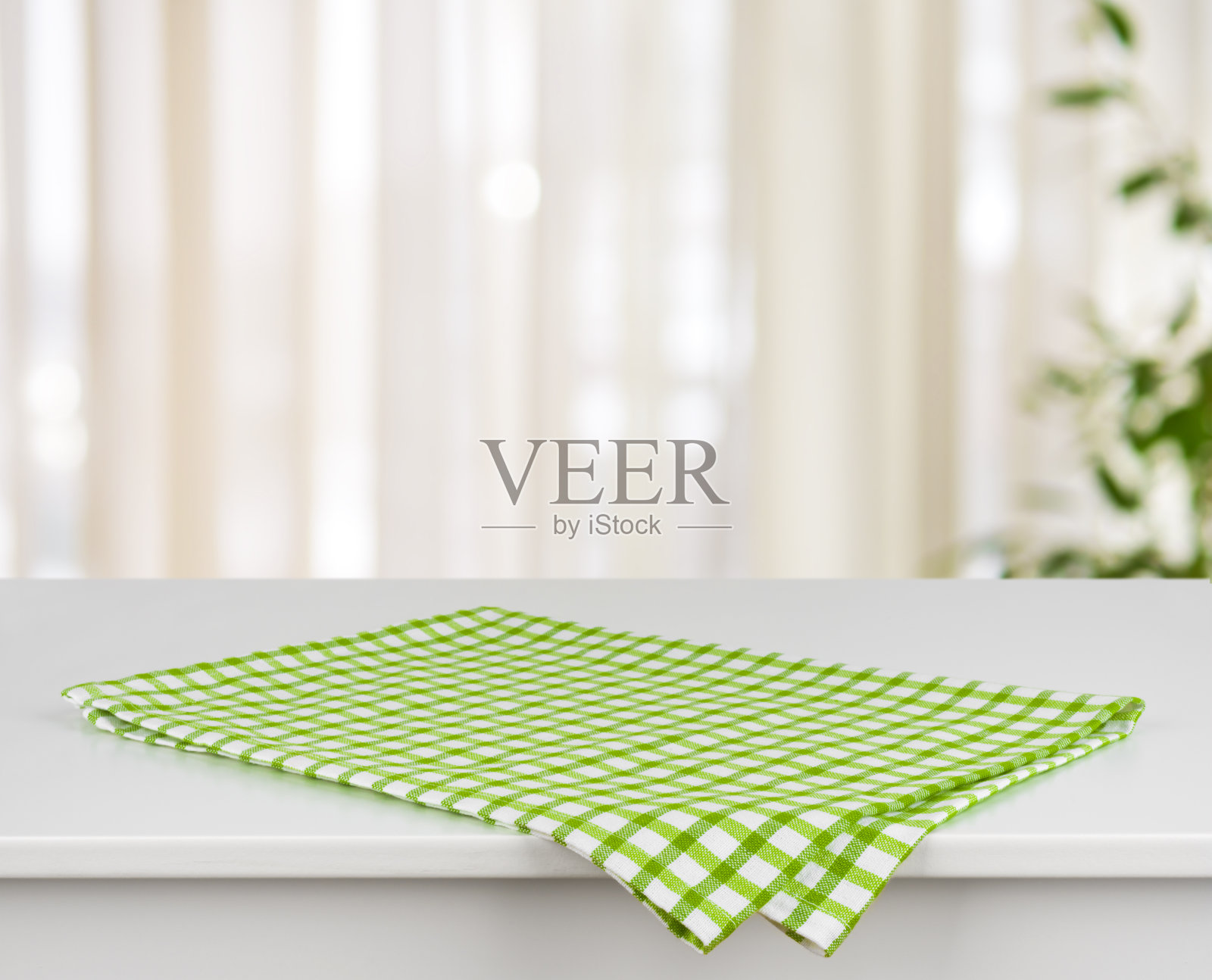 桌子上的绿色格子厨房毛巾，在散焦的窗帘背景上照片摄影图片
