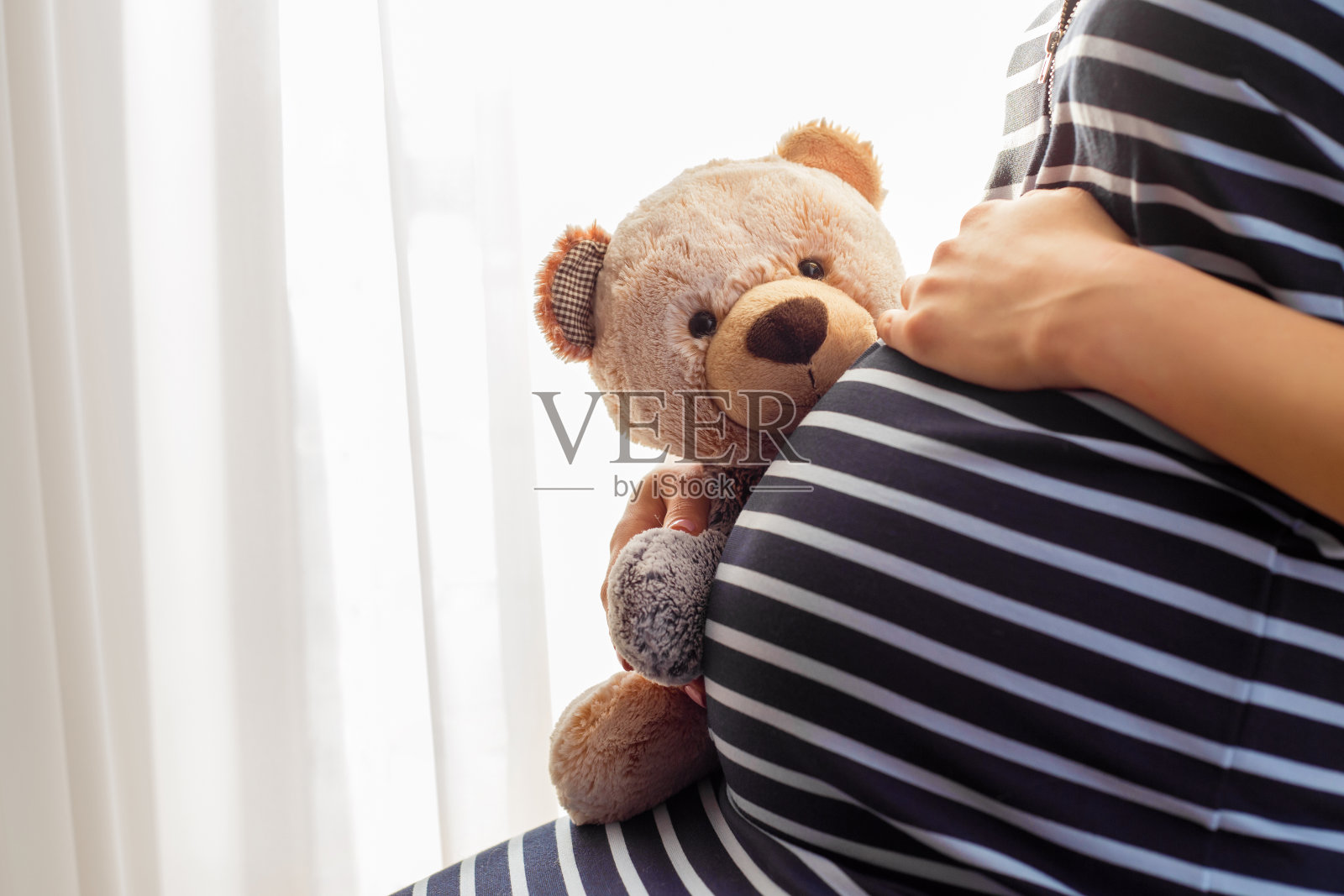 孕妇坐着，抱着泰迪熊玩具照片摄影图片