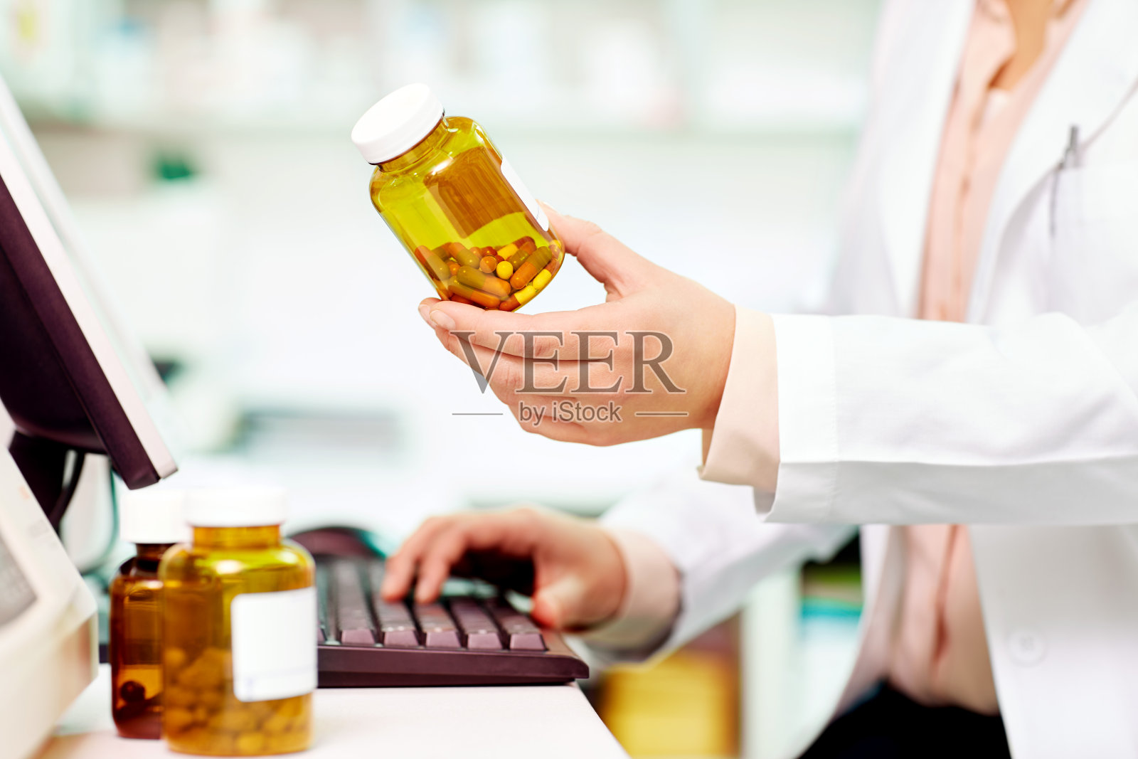 药剂师拿着药瓶站在电脑桌前照片摄影图片