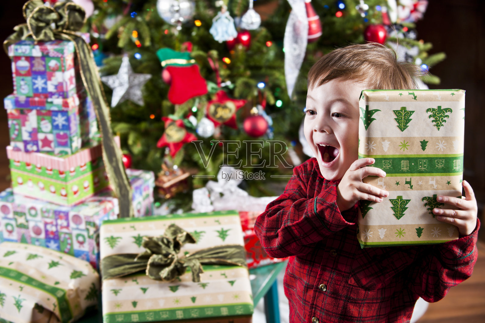 男孩拿着礼物到耳朵前的圣诞树和礼物照片摄影图片