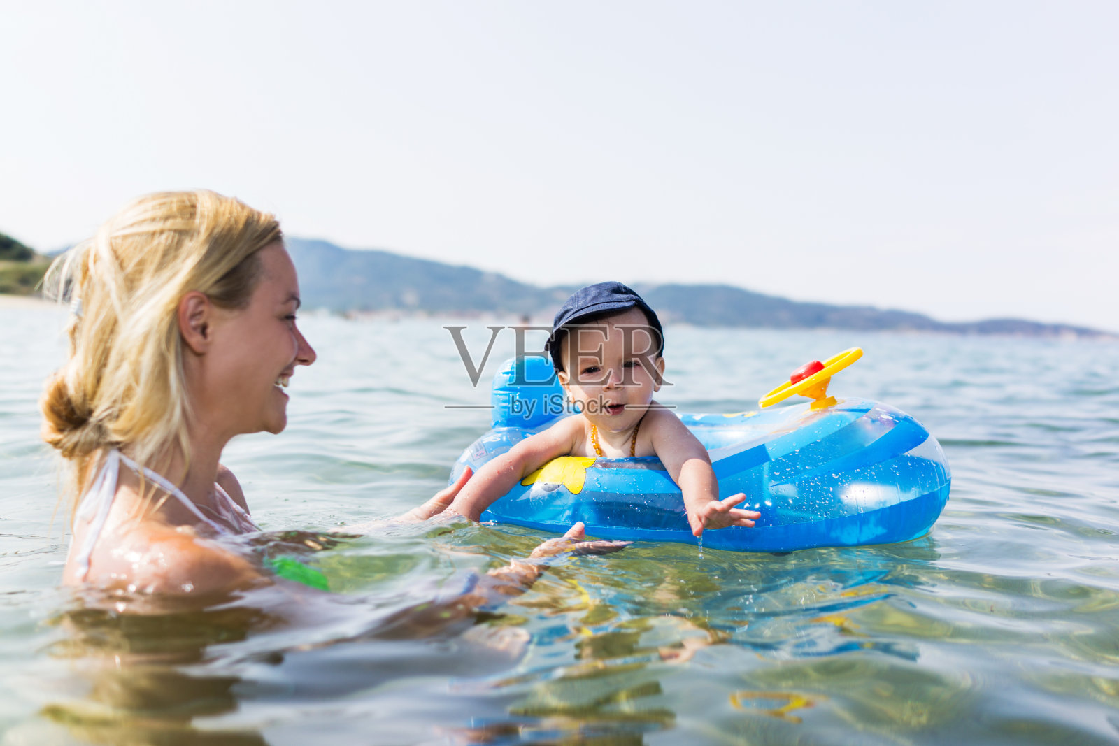 微笑的母亲和蹒跚学步的孩子在海里游泳。照片摄影图片