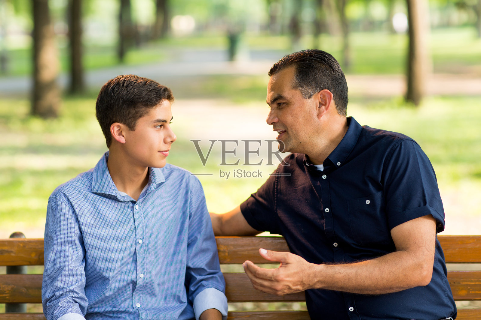 父亲和儿子坐在户外的长椅上照片摄影图片