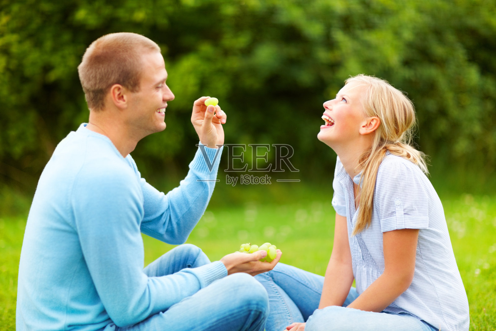 一个快乐的年轻人在公园里把一颗葡萄扔到他女朋友嘴里照片摄影图片