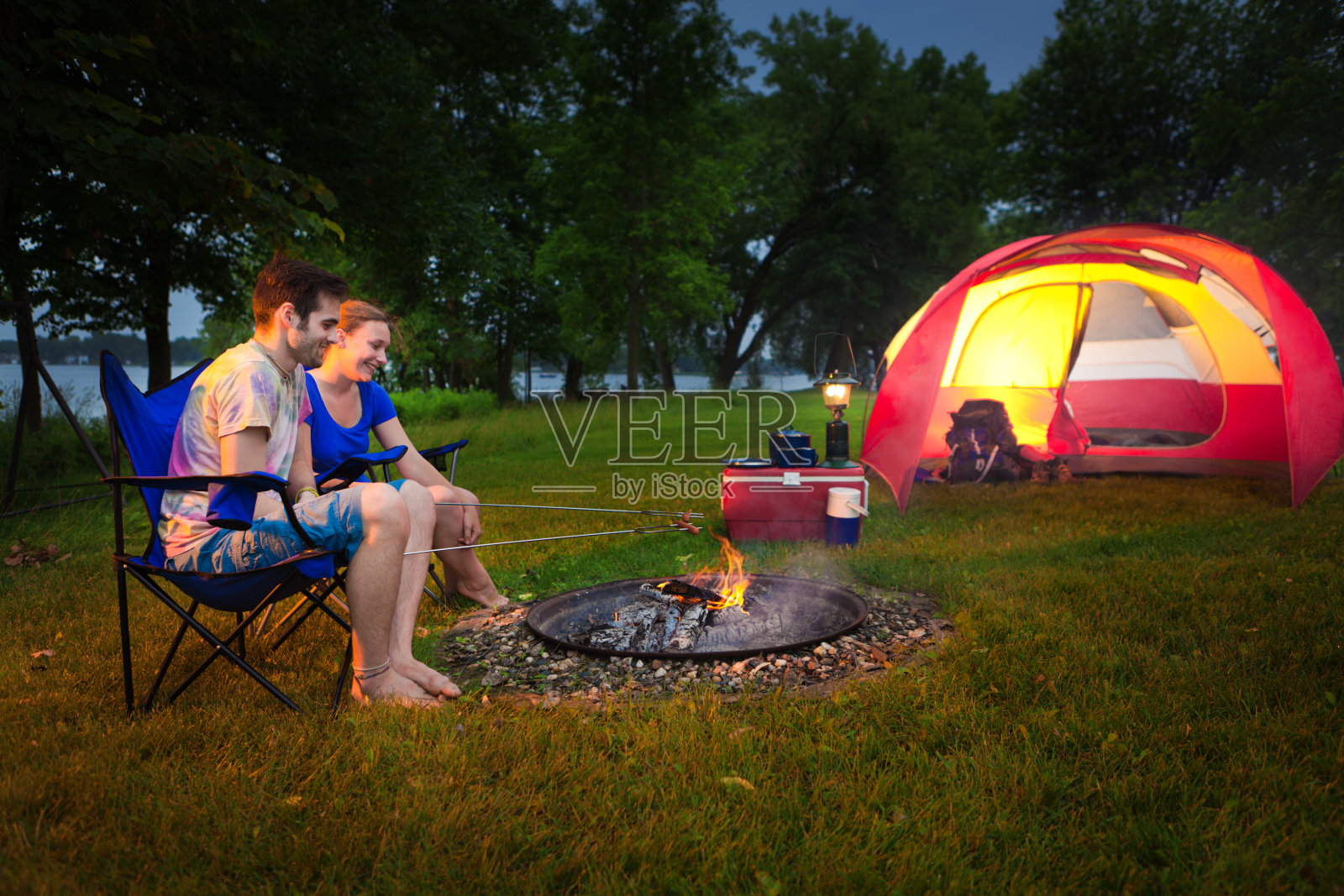一对年轻的夫妇露营在帐篷里，晚上在篝火里烤热狗照片摄影图片