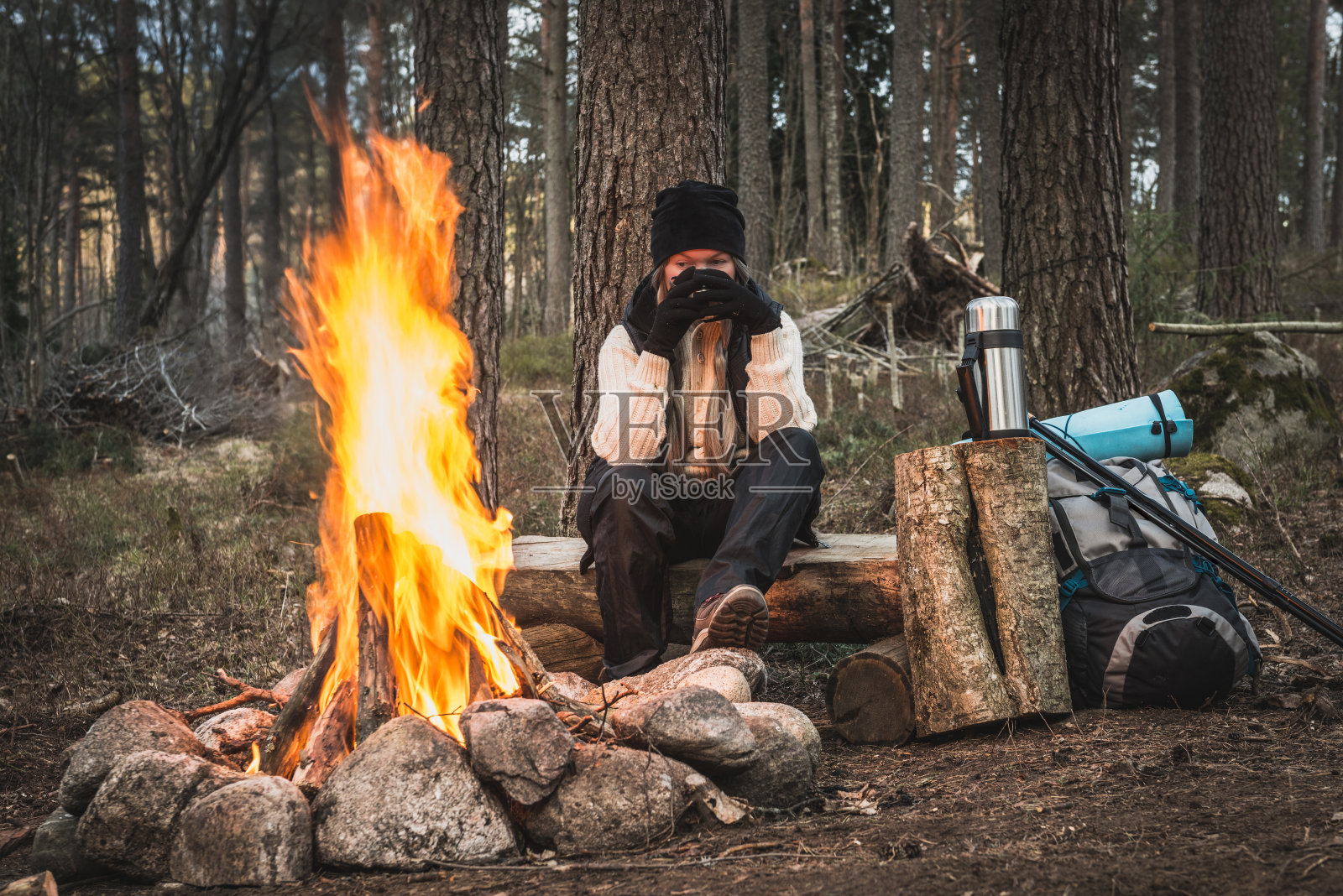 一个女人在篝火旁休息，喝着热饮照片摄影图片