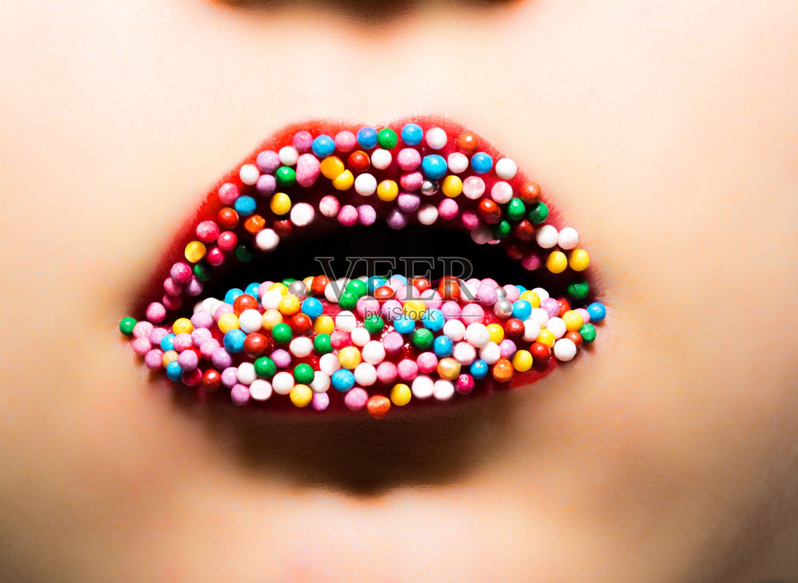 女性的嘴唇涂着红色的口红和五颜六色的糖果。专业化妆女性特写宏。照片摄影图片