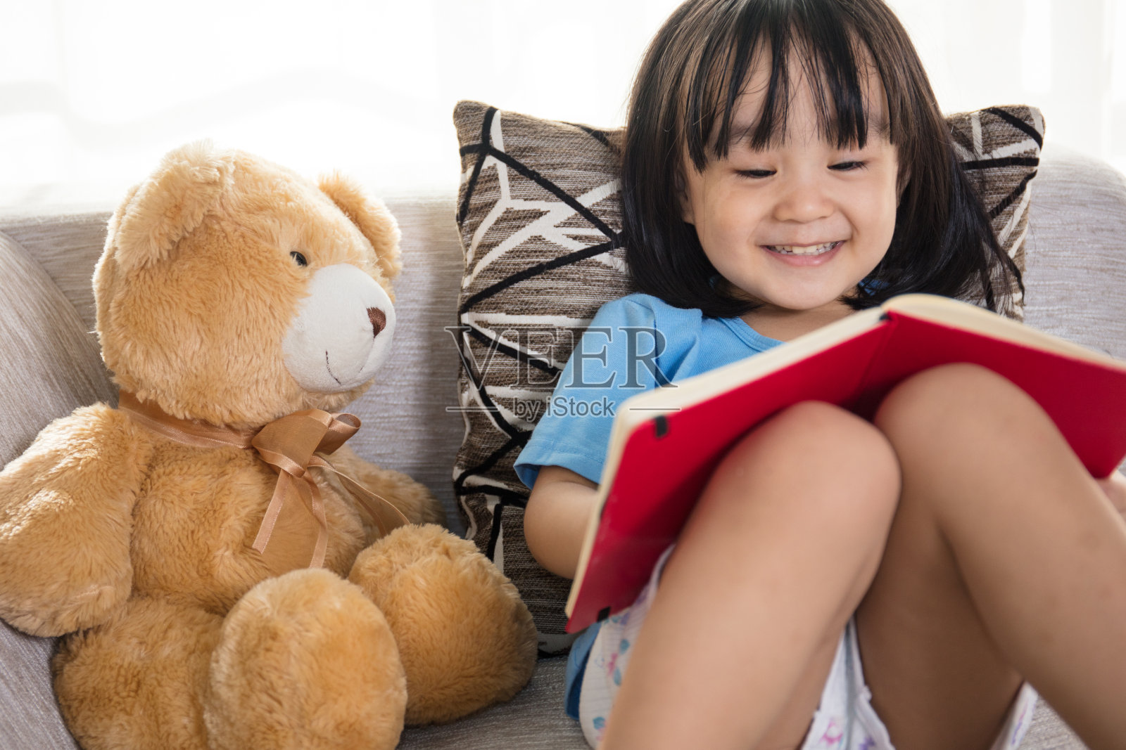 微笑的亚洲华人小女孩和泰迪熊一起看书照片摄影图片