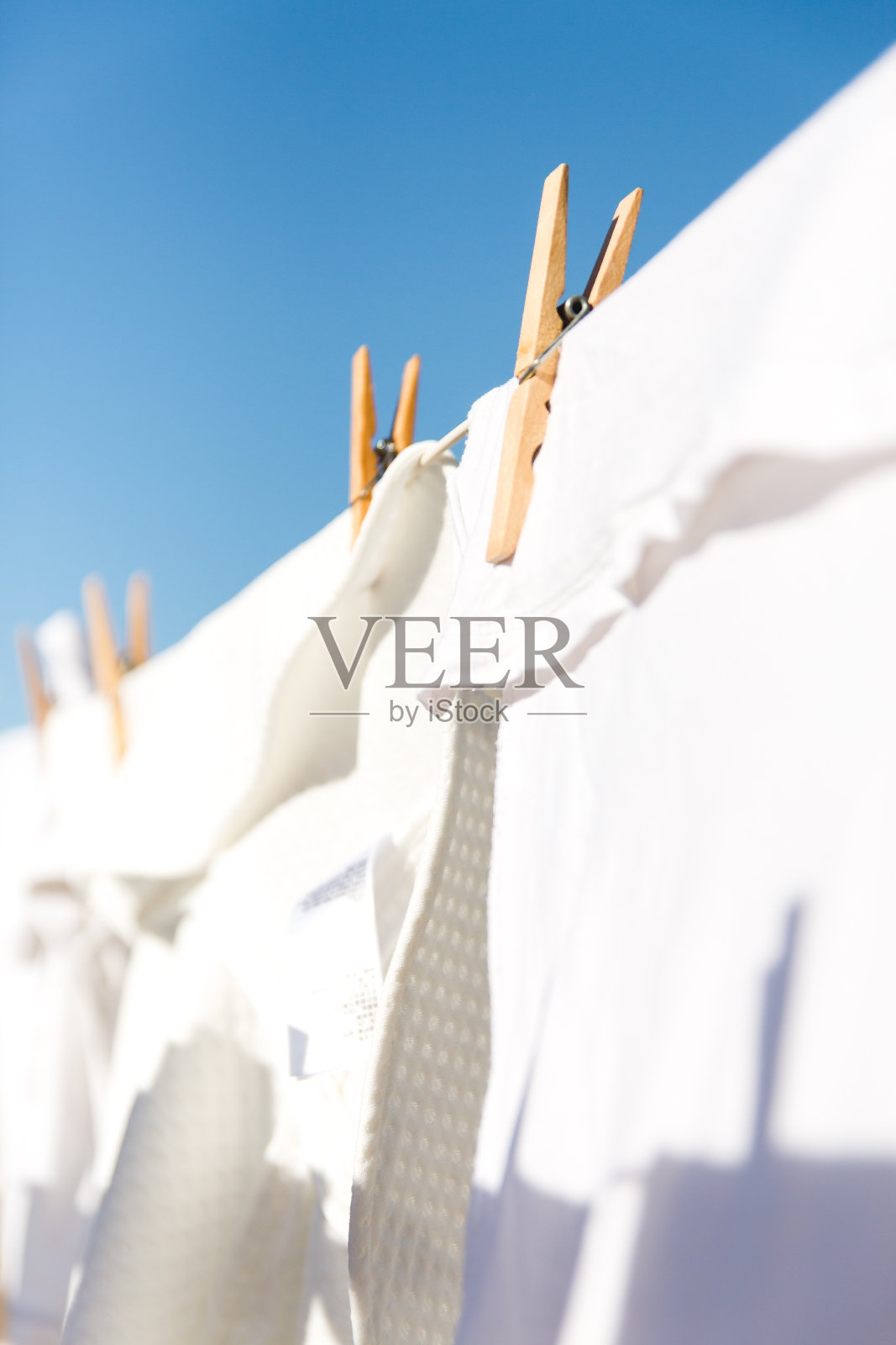 在明亮温暖的阳光下，白色的衣服挂在晾衣绳上晾干。背景是晴朗的蓝天。照片摄影图片