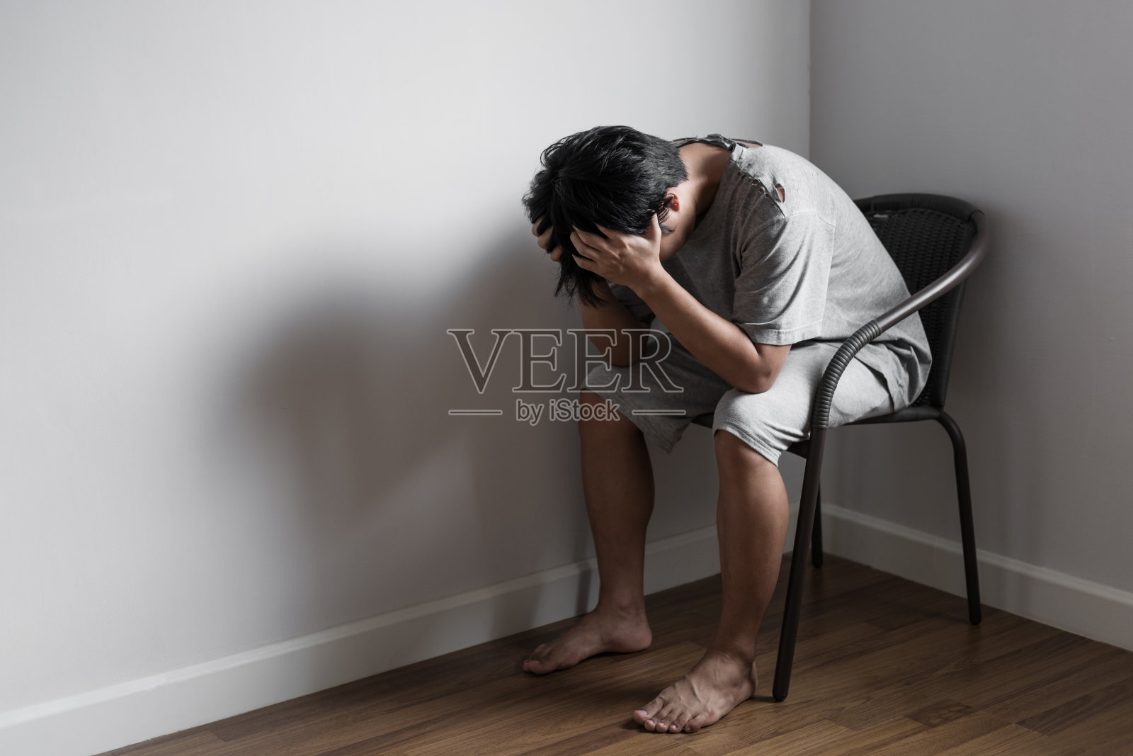 沮丧悲伤可怜的年轻人坐在空房角落的椅子上，悲伤和抑郁的概念照片摄影图片