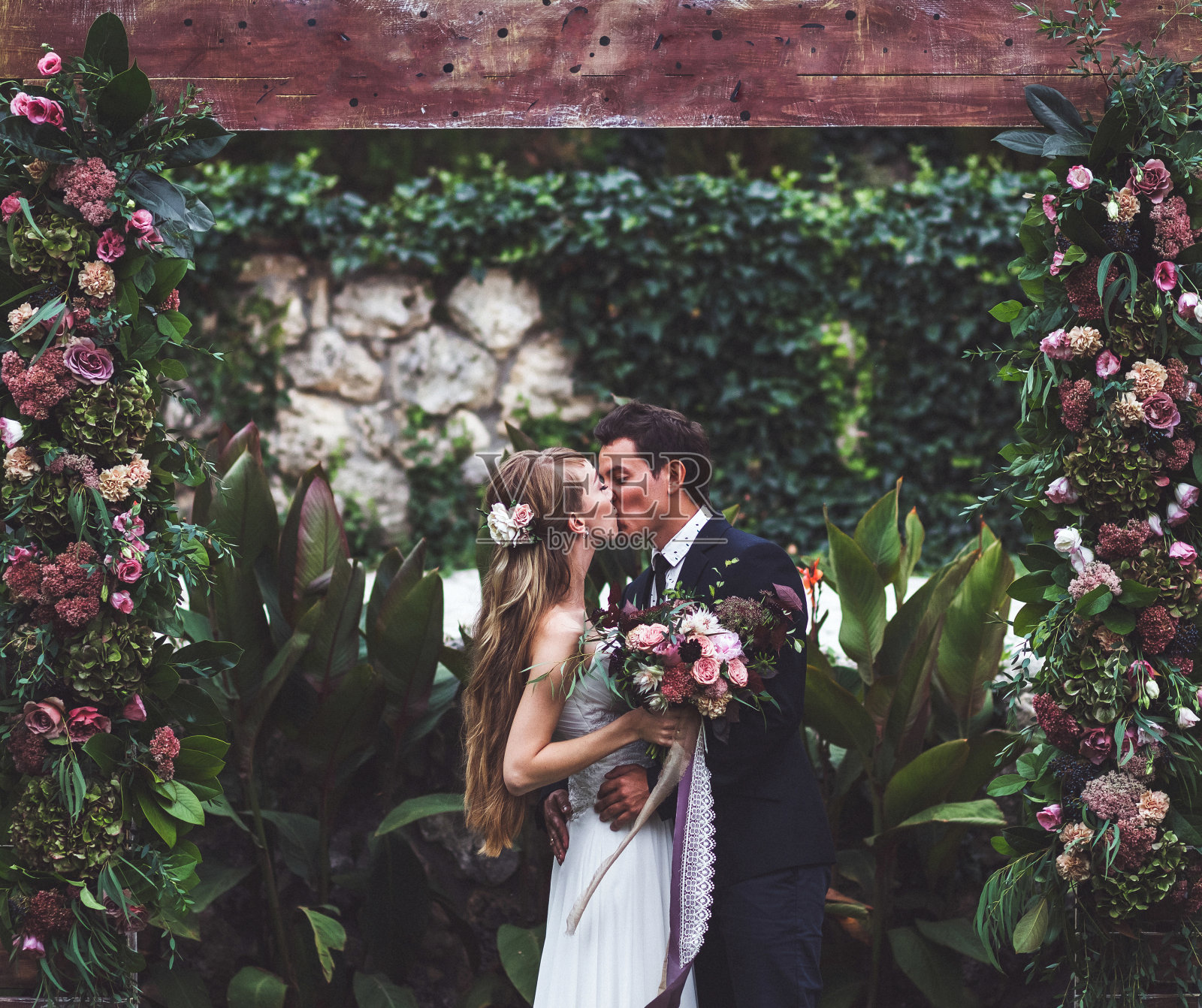 令人惊叹的婚礼上有许多乡村风格的鲜花。幸福的新婚夫妇亲吻照片摄影图片