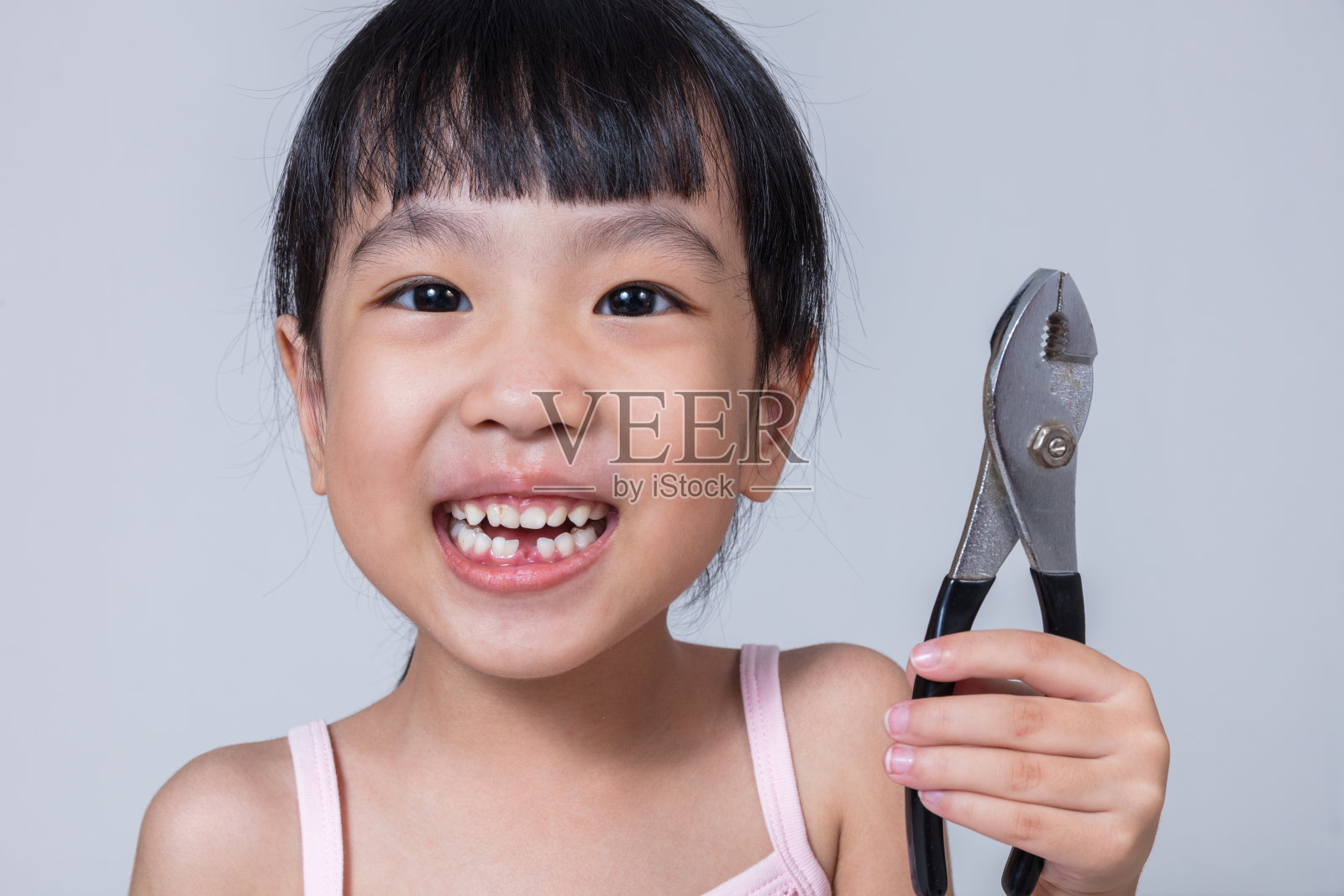亚洲华人小女孩拿着钳子，露出缺口照片摄影图片