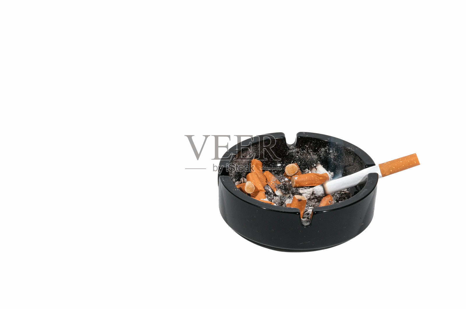 烟灰缸。肮脏的黑色陶瓷烟灰缸里装着一支香烟，里面装满了抽过的香烟。孤立在白色背景上。照片摄影图片