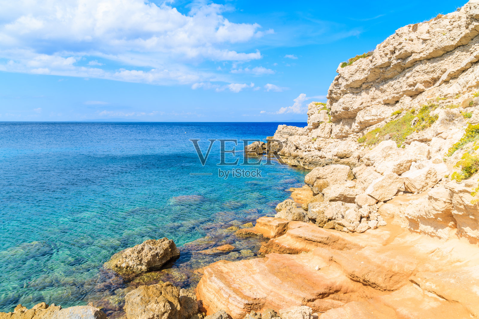 阳光明媚的夏日，希腊萨摩斯岛的Kokkari海湾，岸边的岩石和湛蓝的海水照片摄影图片