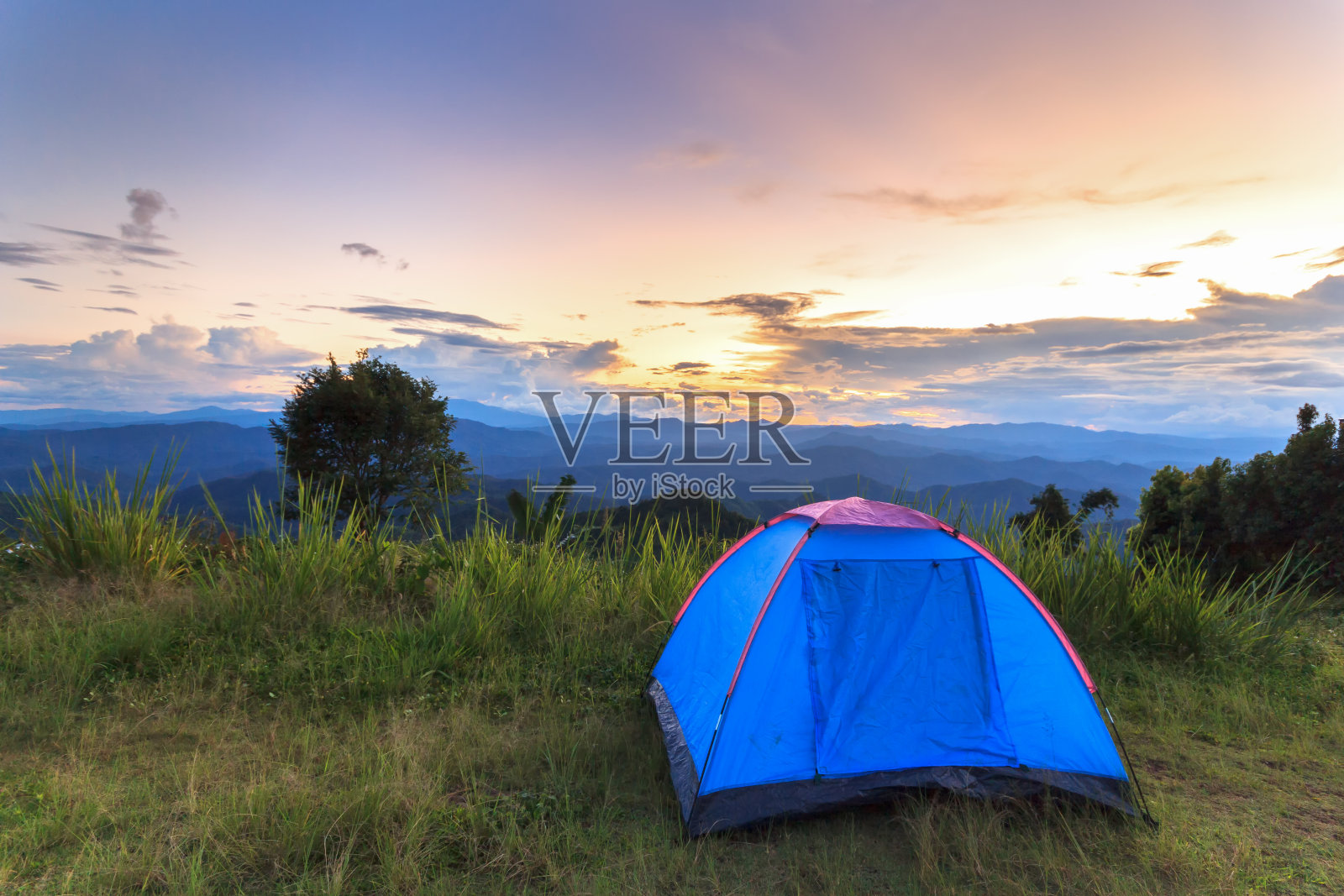 蓝色帐篷站在山顶的草地上，夕阳西下照片摄影图片