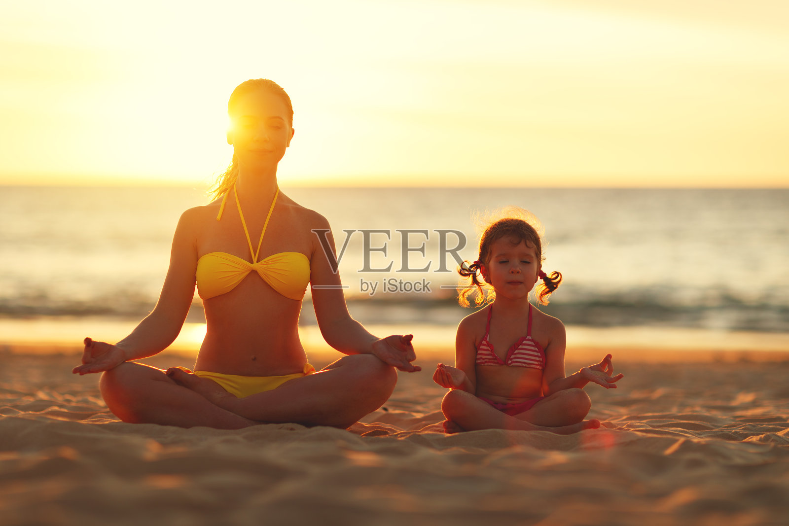 幸福的家庭妈妈和孩子做瑜伽，在沙滩上莲花姿势冥想照片摄影图片