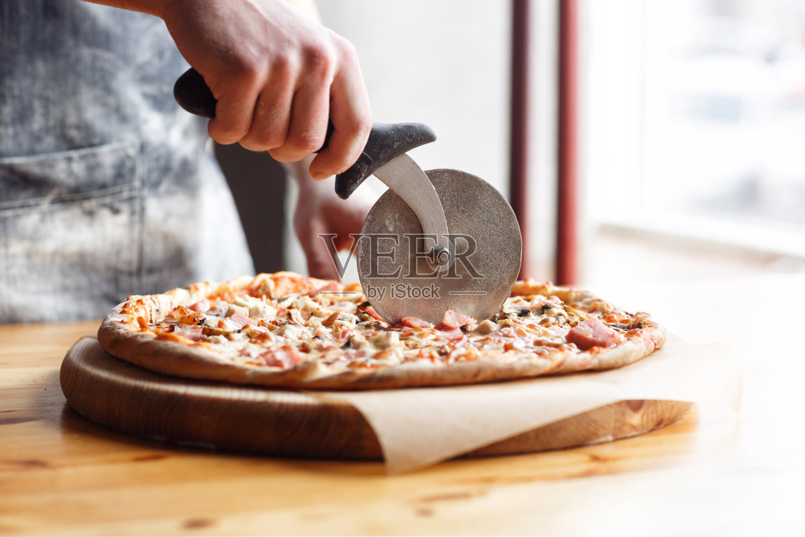 在厨房切披萨的厨师在蓝色围裙的特写手照片摄影图片