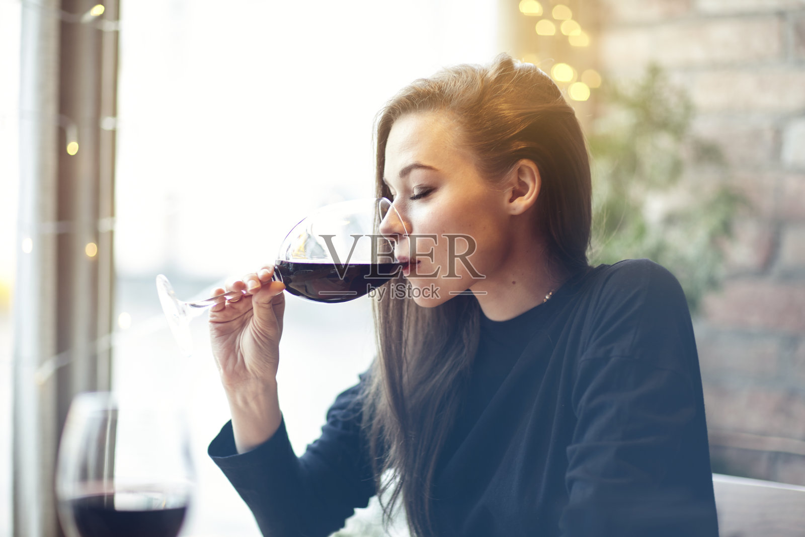 美丽的年轻女子喝红酒与朋友在咖啡馆，肖像与葡萄酒杯靠近窗户。假期假期晚上概念照片摄影图片