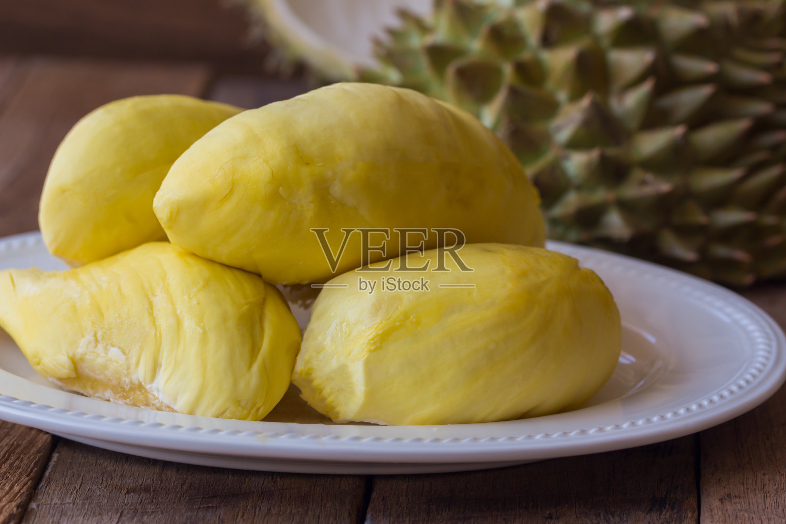 泰国传统水果:泰国水果之王榴莲放在白色盘子上，放在质朴的木桌上。榴莲是热带水果，很好吃，很甜，很香。成熟的榴莲呈金黄色。照片摄影图片