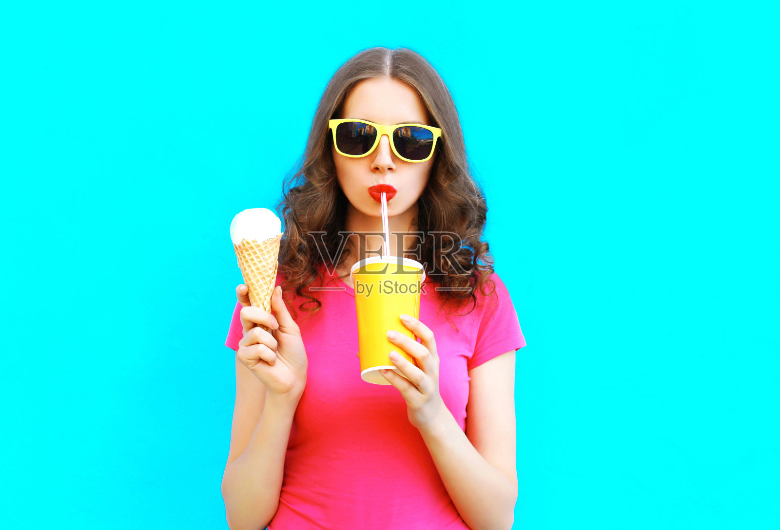 时尚肖像女人喝果汁从杯子和持有冰淇淋在彩色的蓝色背景照片摄影图片