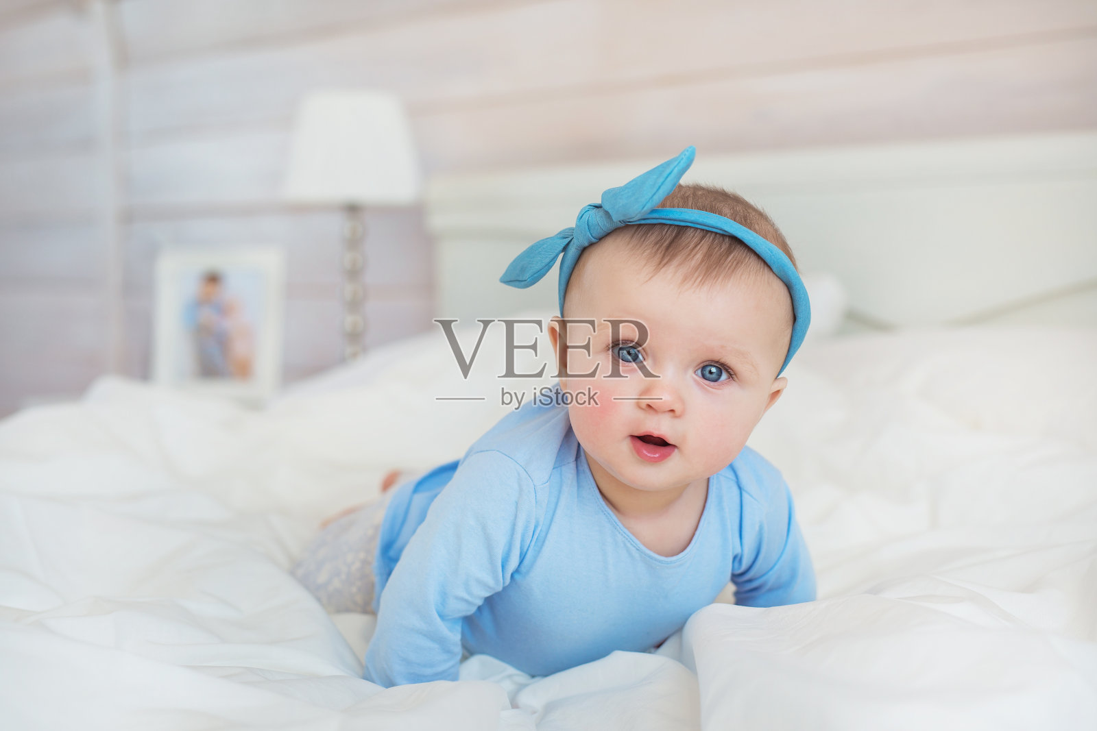 蓝色衣服的婴儿微笑着爬在卧室的床上照片摄影图片