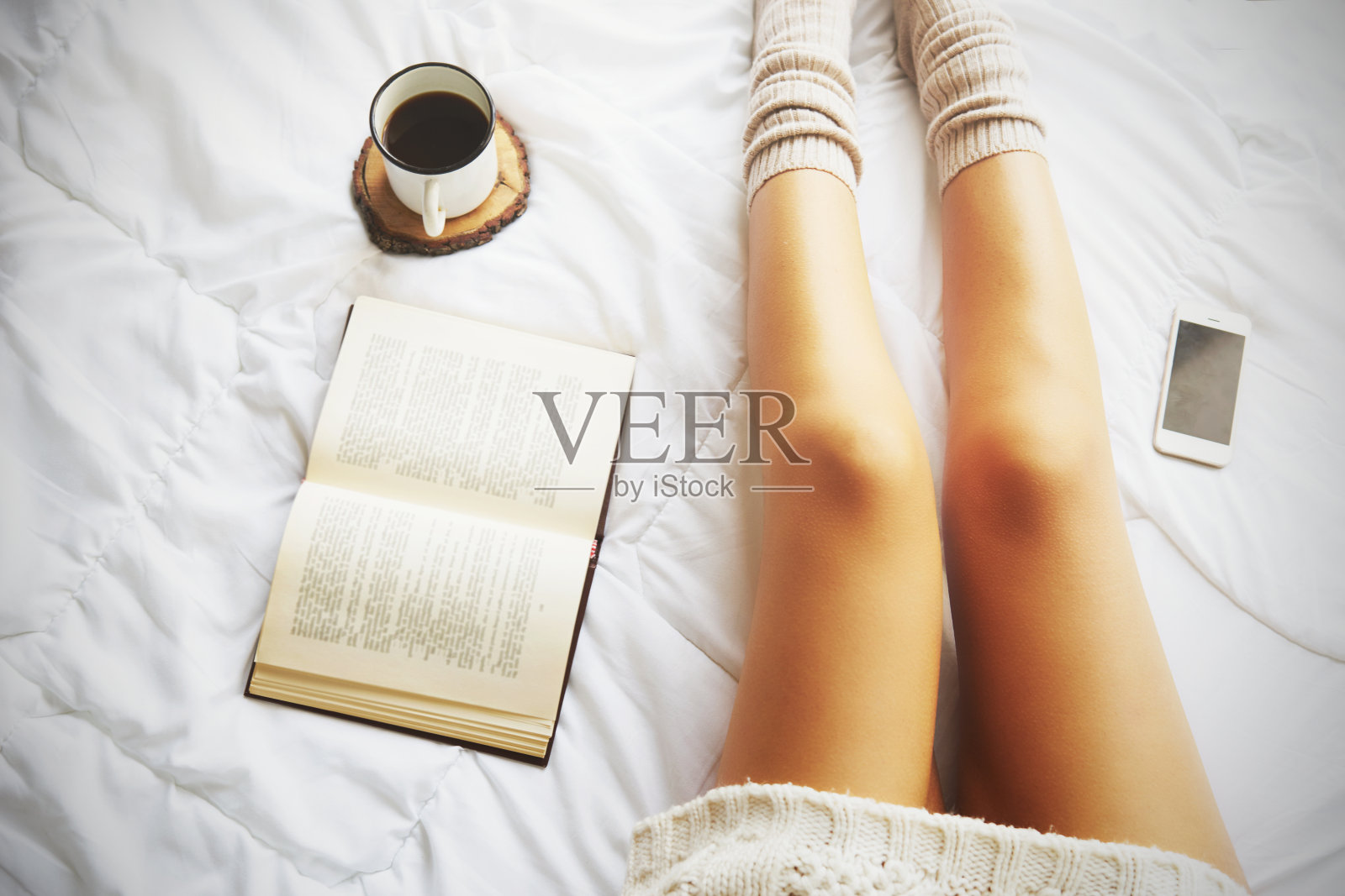 软照片的女人在床上与书和一杯咖啡，俯视图照片摄影图片