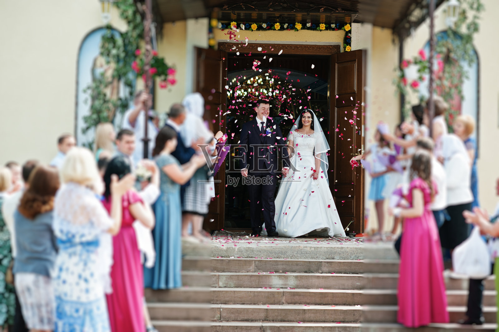 出教堂时，客人们用玫瑰花瓣迎接新婚夫妇。照片摄影图片