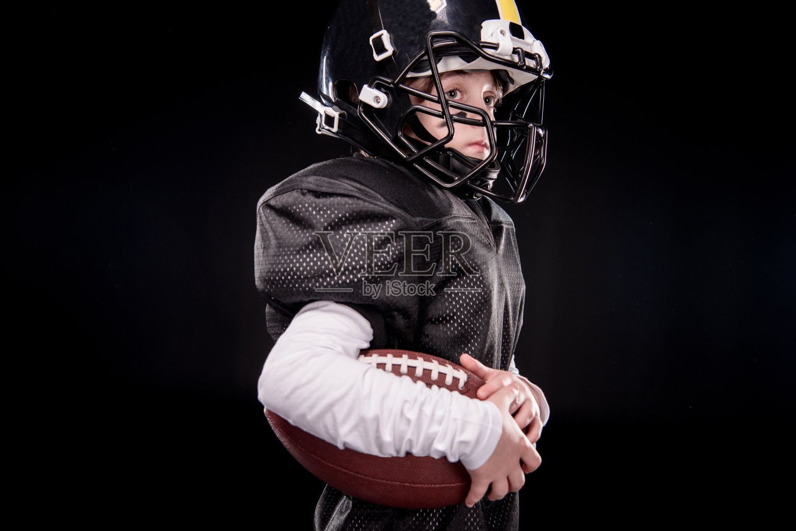 侧面的小男孩美国足球运动员在黑色的制服持有球照片摄影图片