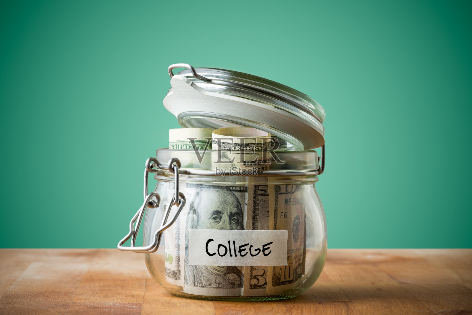 在绿色背景上孤立的玻璃罐中的美元。为上大学省钱的概念。照片摄影图片