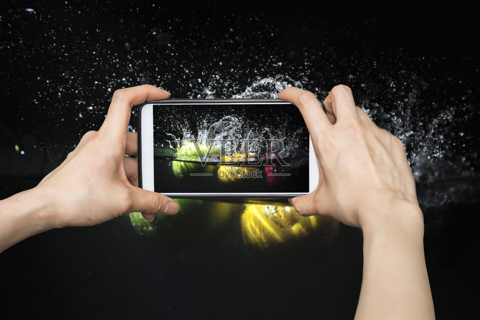 用智能手机拍照，把水果泼到水里。黑色背景的新鲜水果照片摄影图片