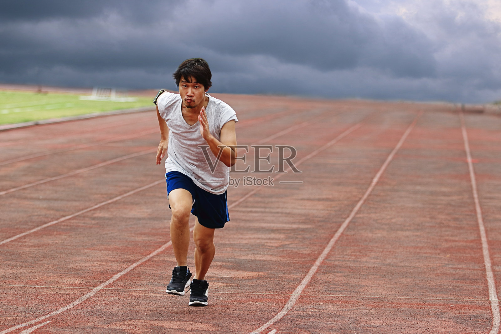 年轻的亚洲选手在天气风暴背景下的赛道上跑步。照片摄影图片