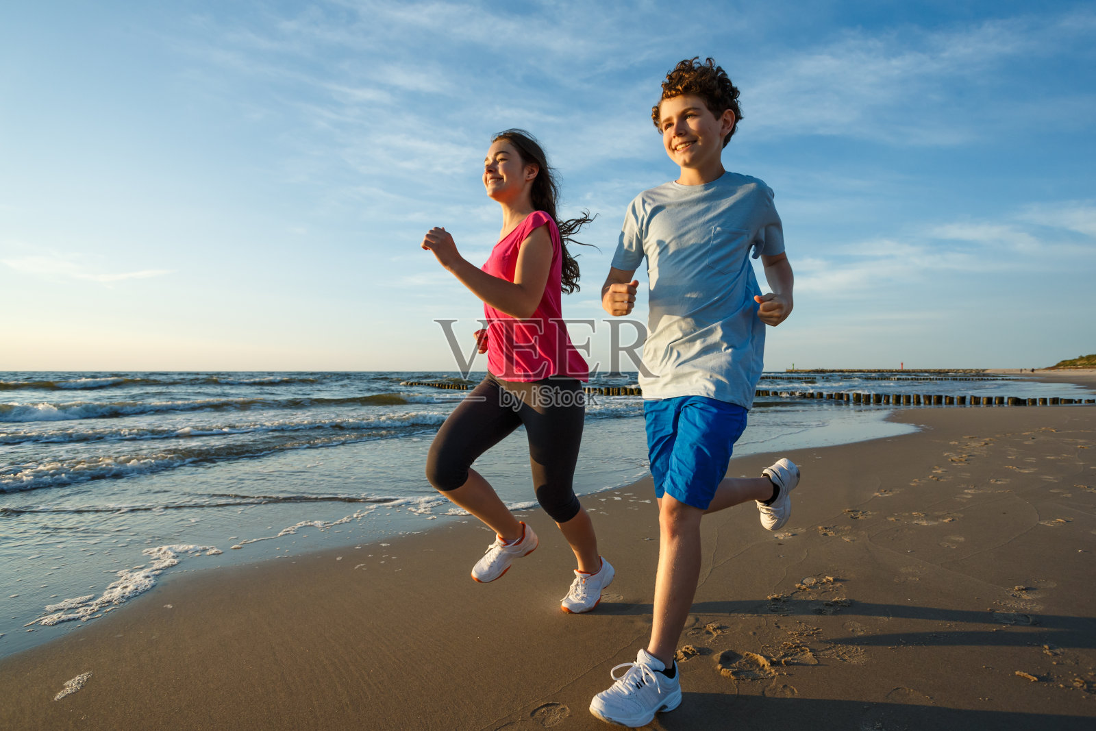 十几岁的女孩和男孩在海滩上奔跑跳跃照片摄影图片
