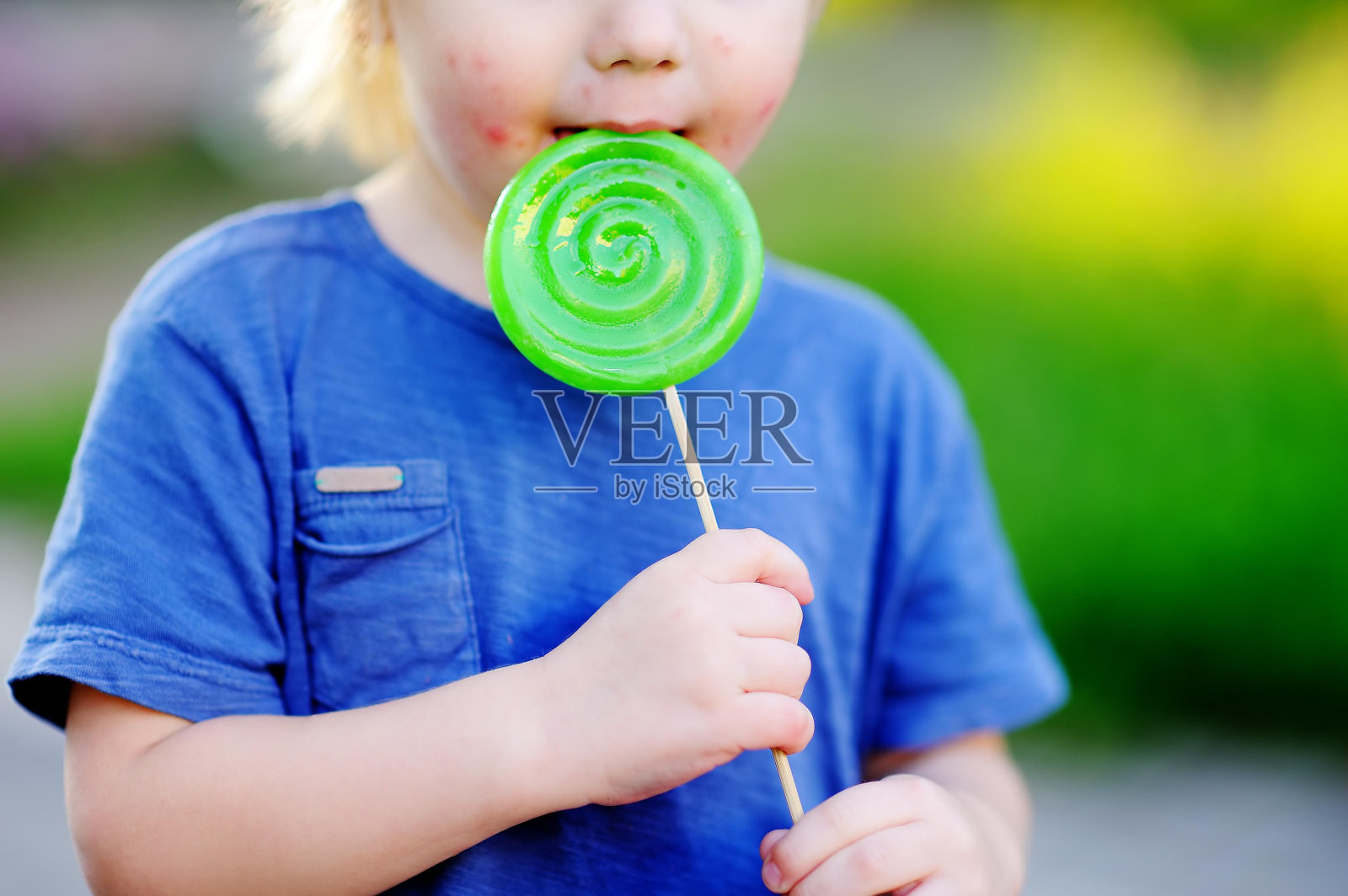 有过敏反应的孩子吃了大的绿色棒棒糖照片摄影图片