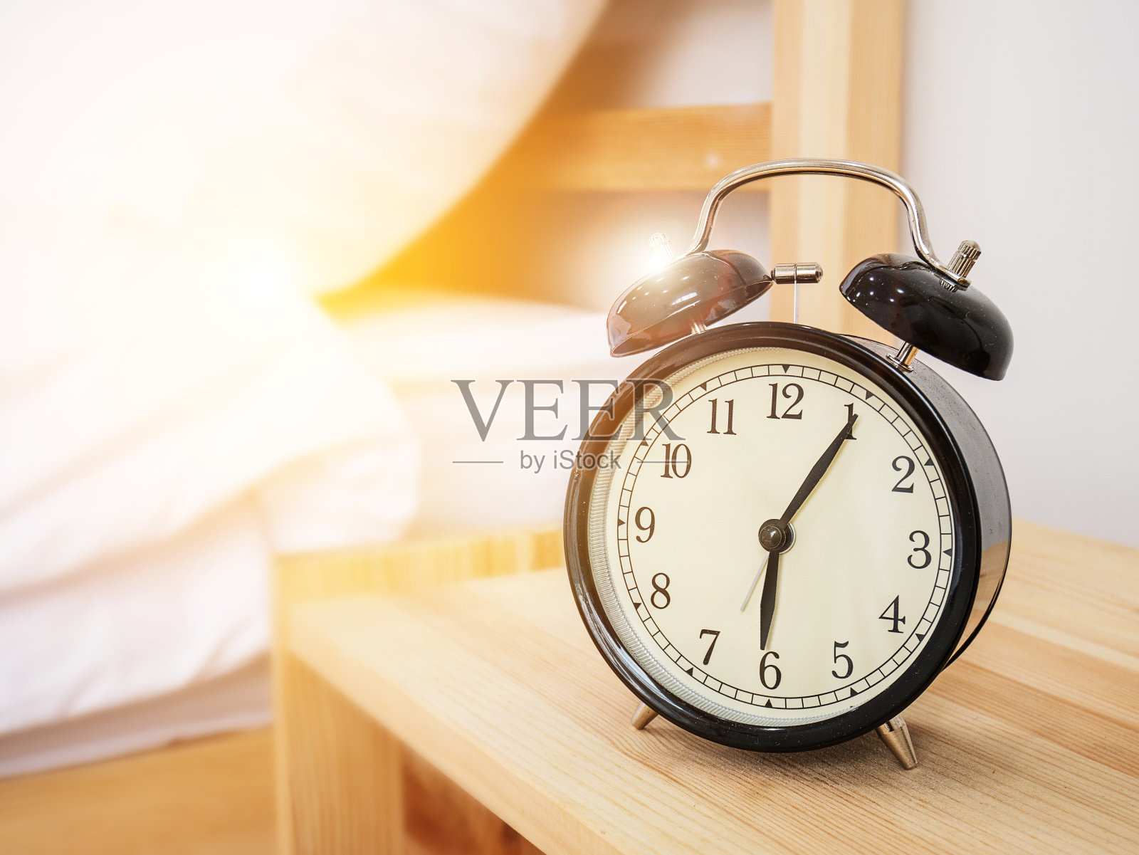 闹钟，起床时间概念:复古闹钟在早上六点过五分钟，木制的床边桌子，白色的床单和早晨的阳光背景照片摄影图片
