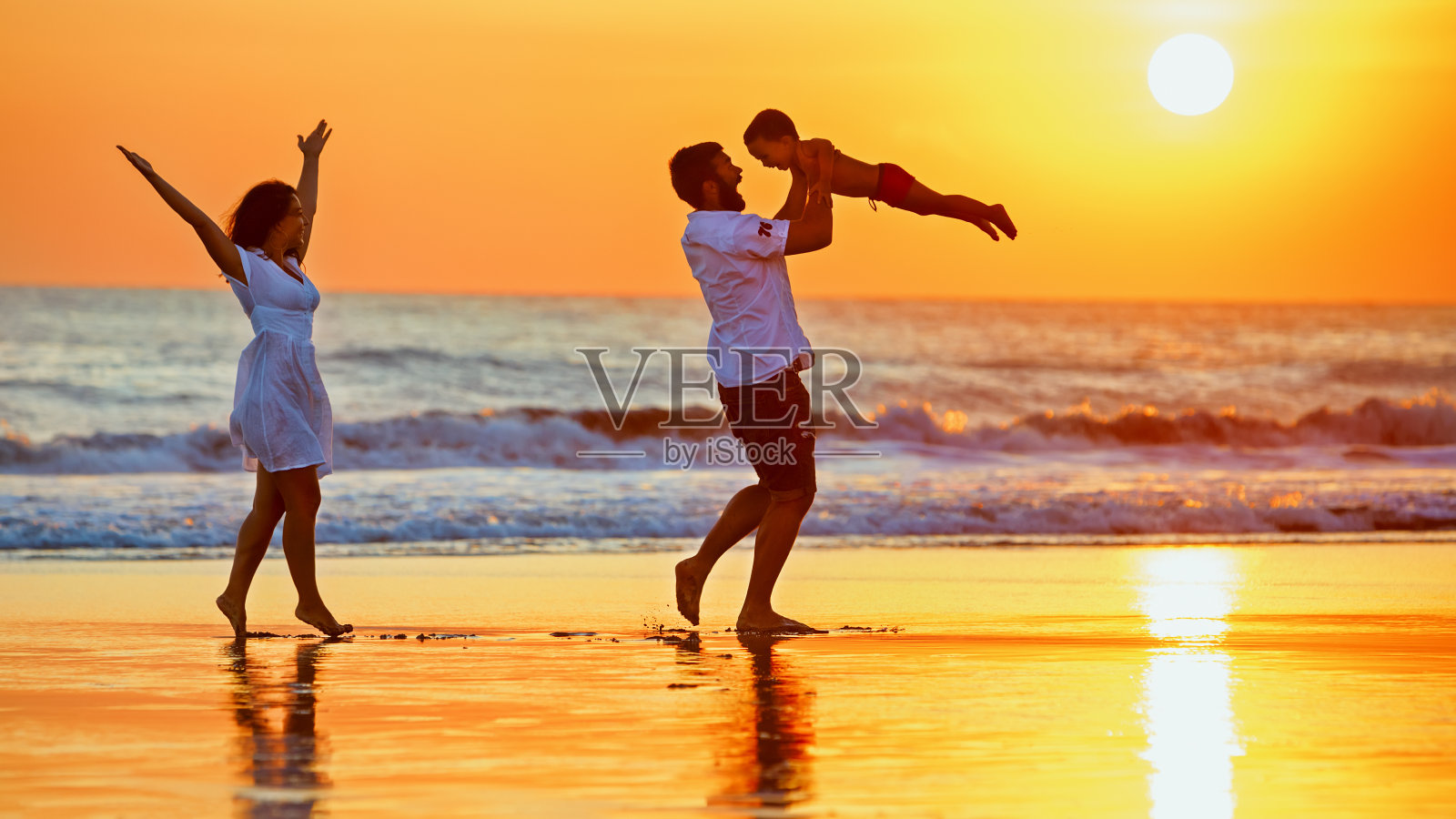 快乐的家庭漫步在日落的海滩上照片摄影图片