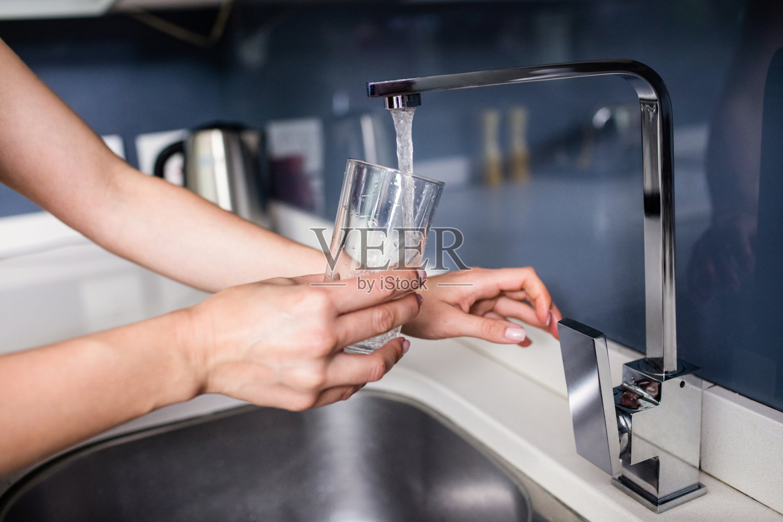 在厨房水槽往玻璃杯里注水的女人照片摄影图片
