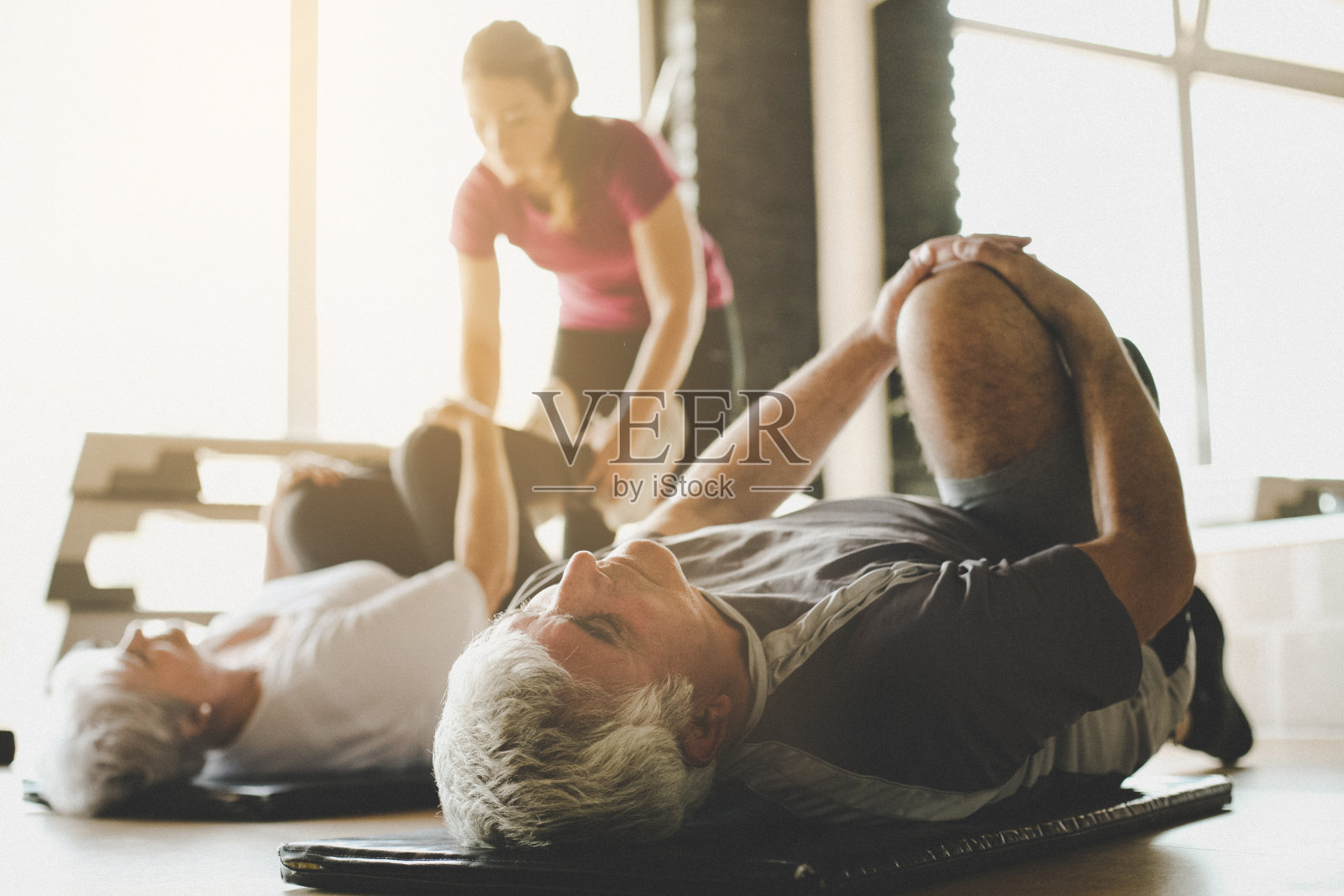 老年夫妇在康复中心锻炼。私人教练帮助老夫妇在地板上做伸展运动。关注的人。照片摄影图片