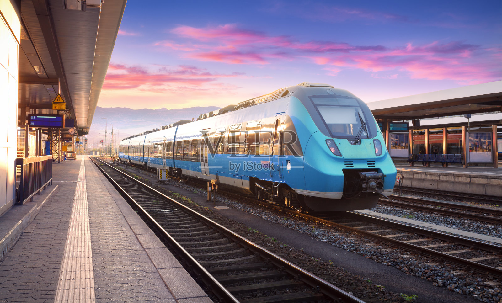 美丽的风景与现代的通勤列车在火车站和彩色天空与云彩日落在欧洲。蓝色火车站台的工业景观。铁路的背景照片摄影图片