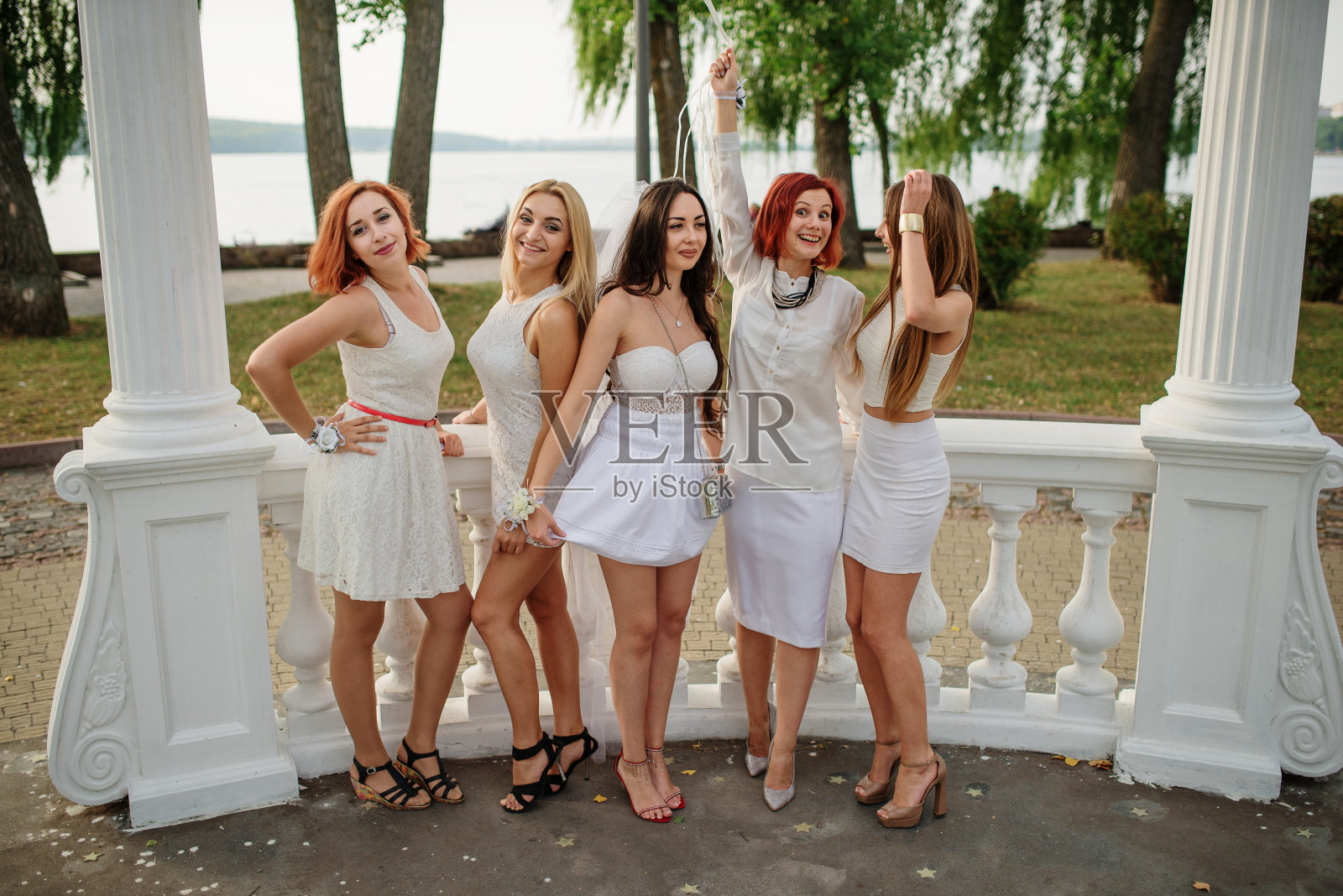 五个手里拿着气球的女孩穿着白色的衣服，在白色的拱门柱旁参加女性聚会。照片摄影图片